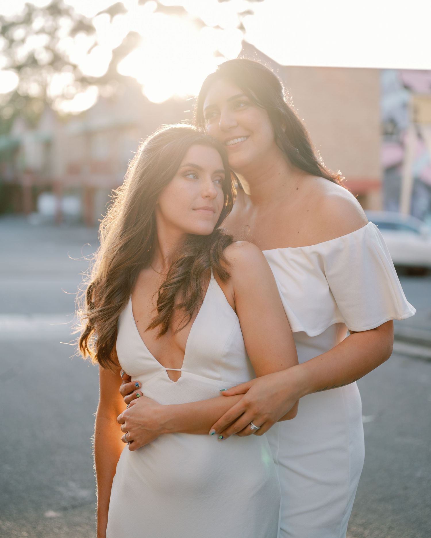 Couple embracing in white outfits during golden hour sunset photoshoot.