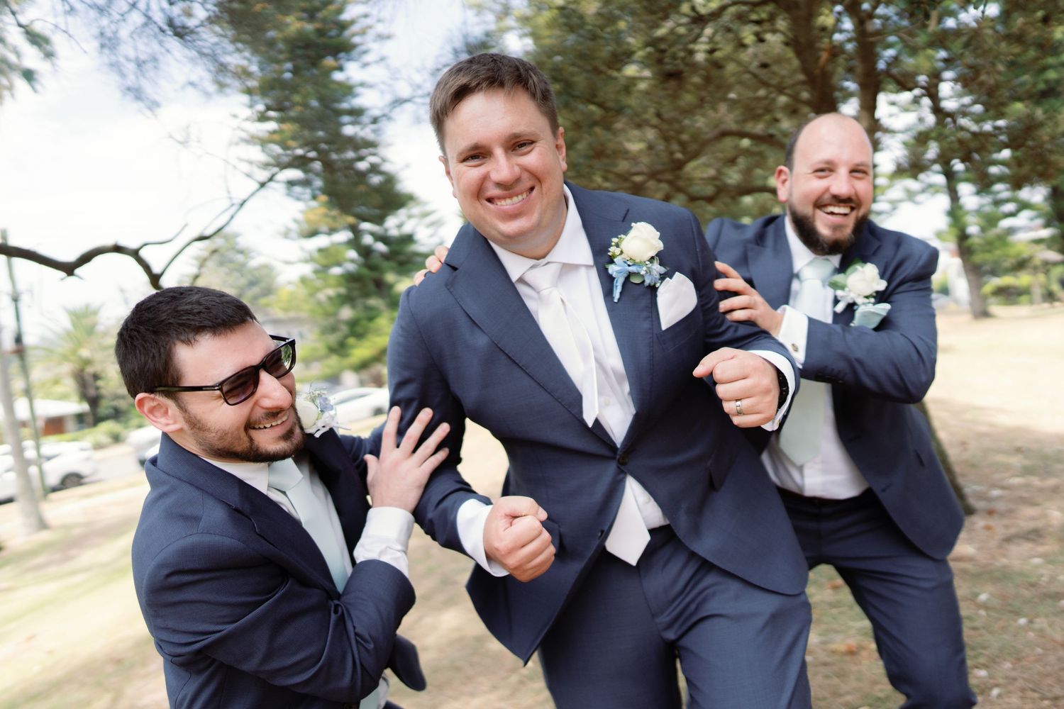 Groomsmen in navy suits sharing laughs and playful moments outdoors.