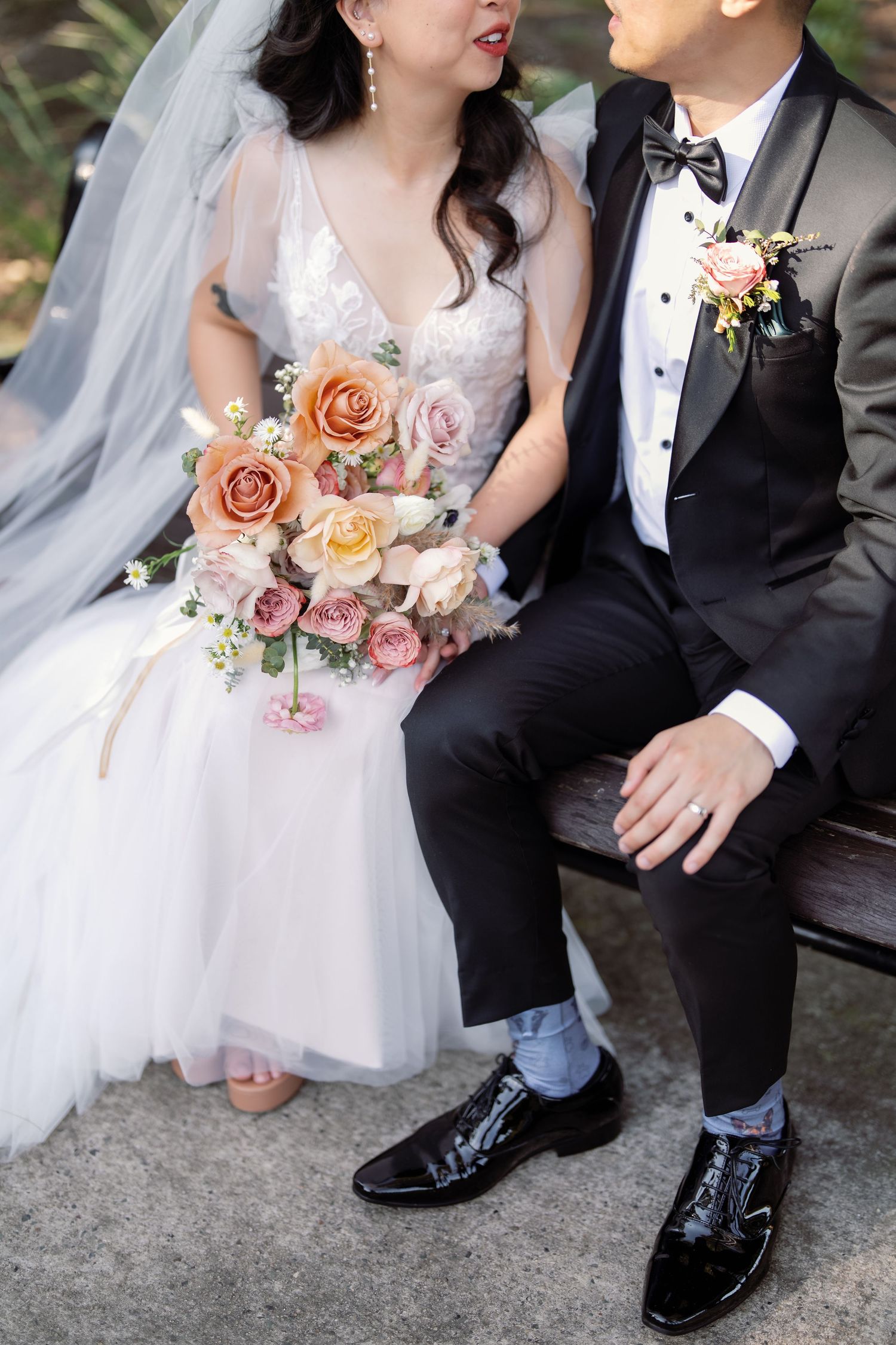 Close-up of wedding attire with a peach and pink rose bouquet.