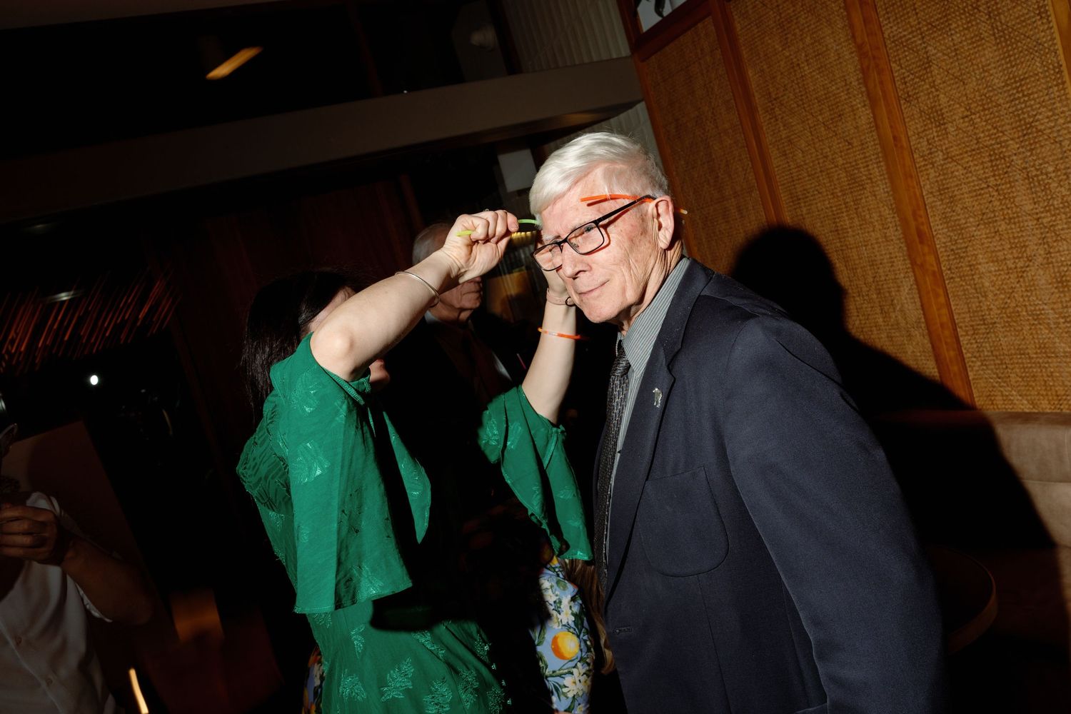 Older man in gray suit adjusting glasses while smiling at formal event.