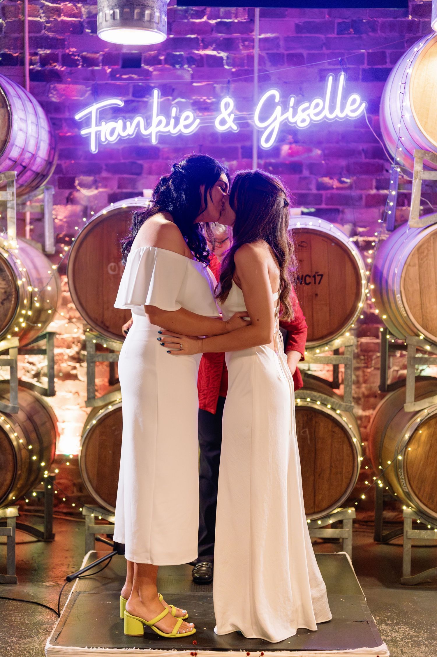 Wedding celebration in a wine cellar with wooden barrels and purple neon lighting.