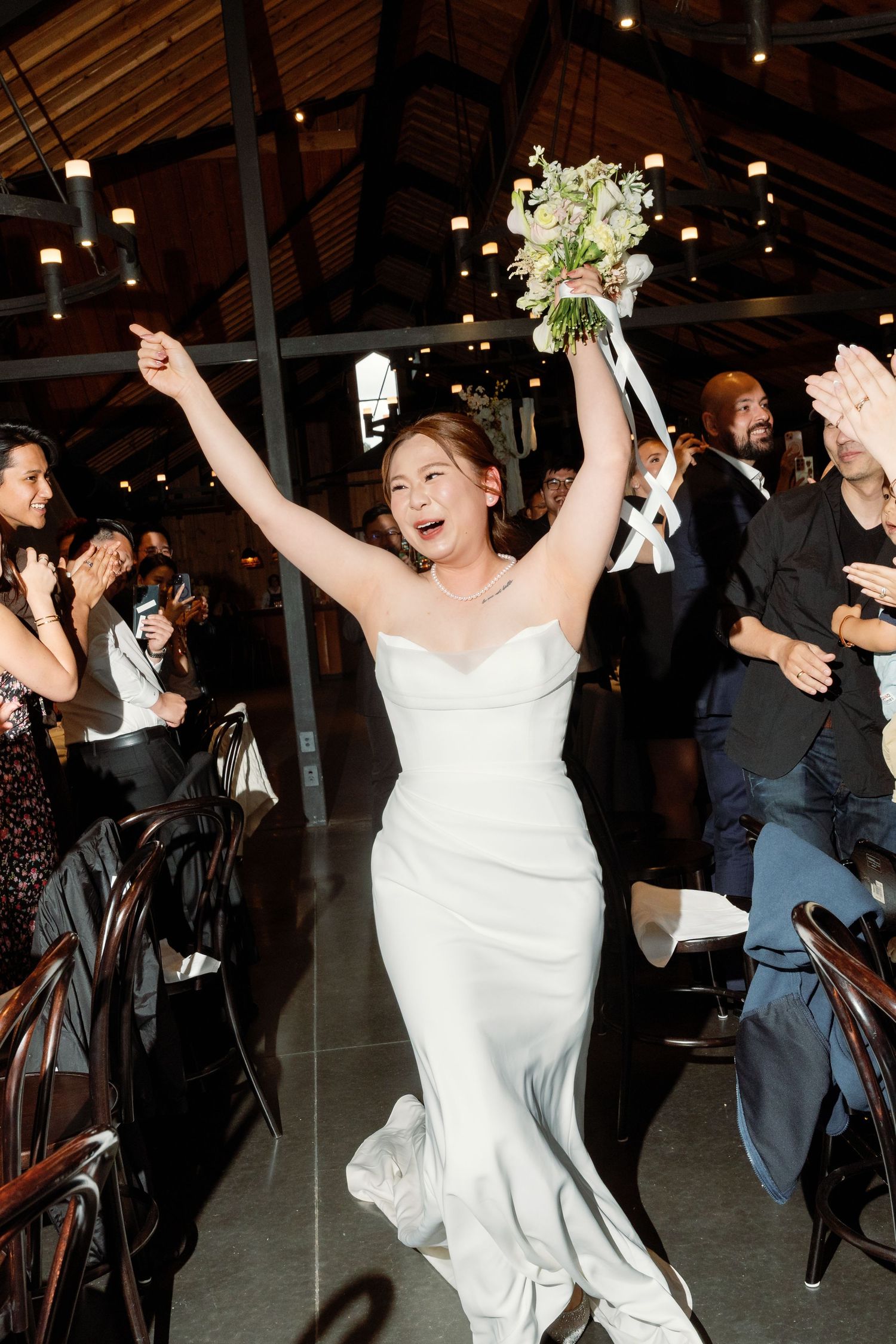 Bride celebrates joyfully on dance floor during wedding reception in rustic venue.