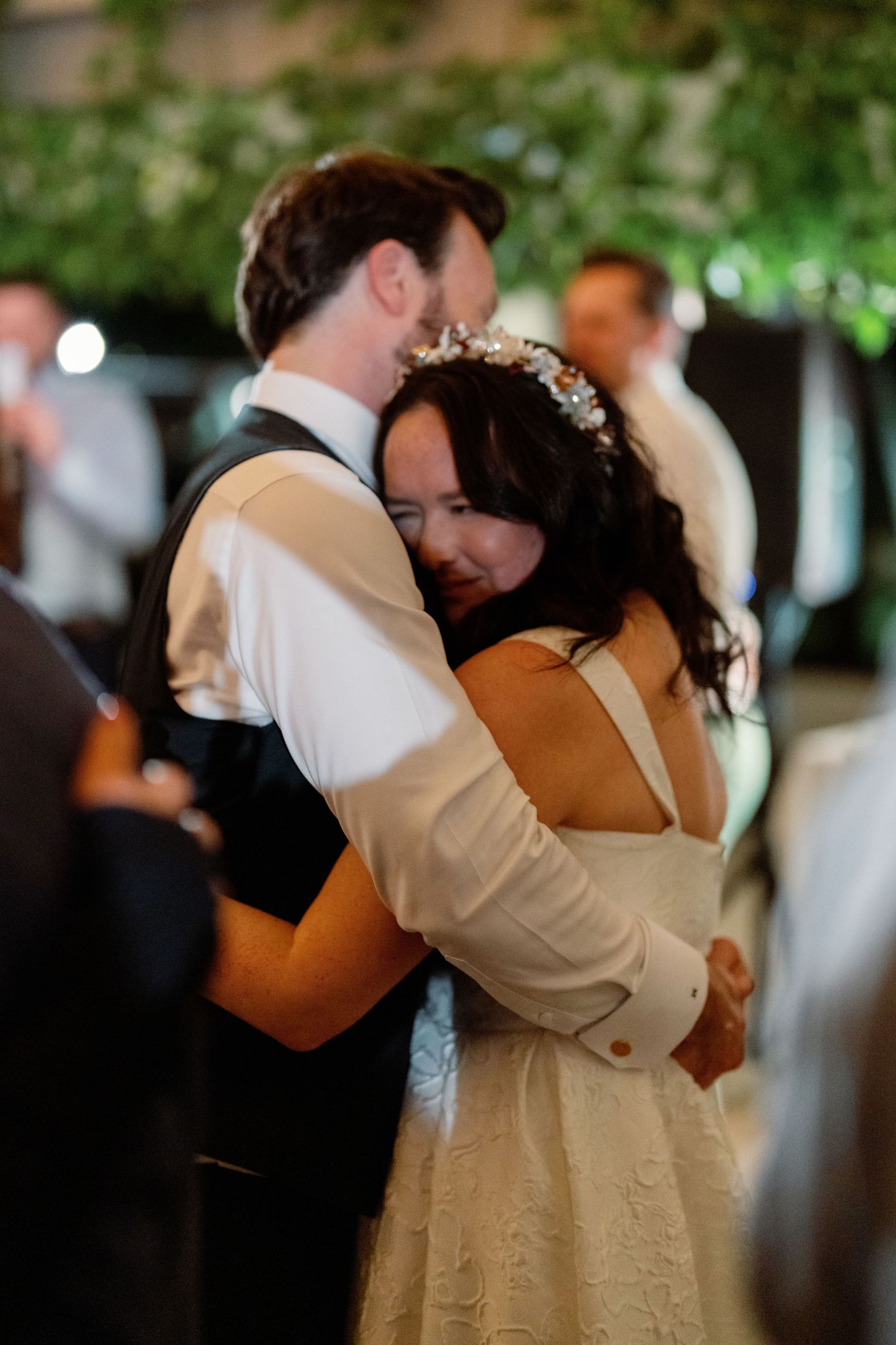 Bride and groom sharing emotional first dance embrace at wedding reception surrounded by greenery decor.
