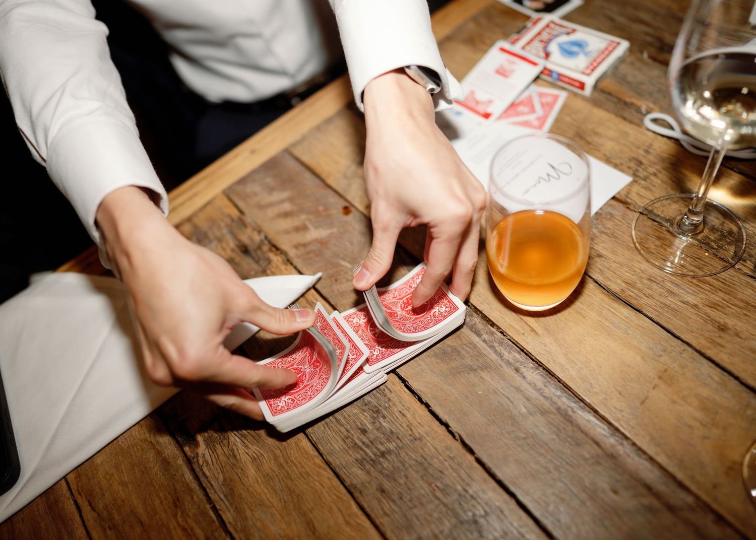 Close-up of hands playing cards at wooden table with drinks.