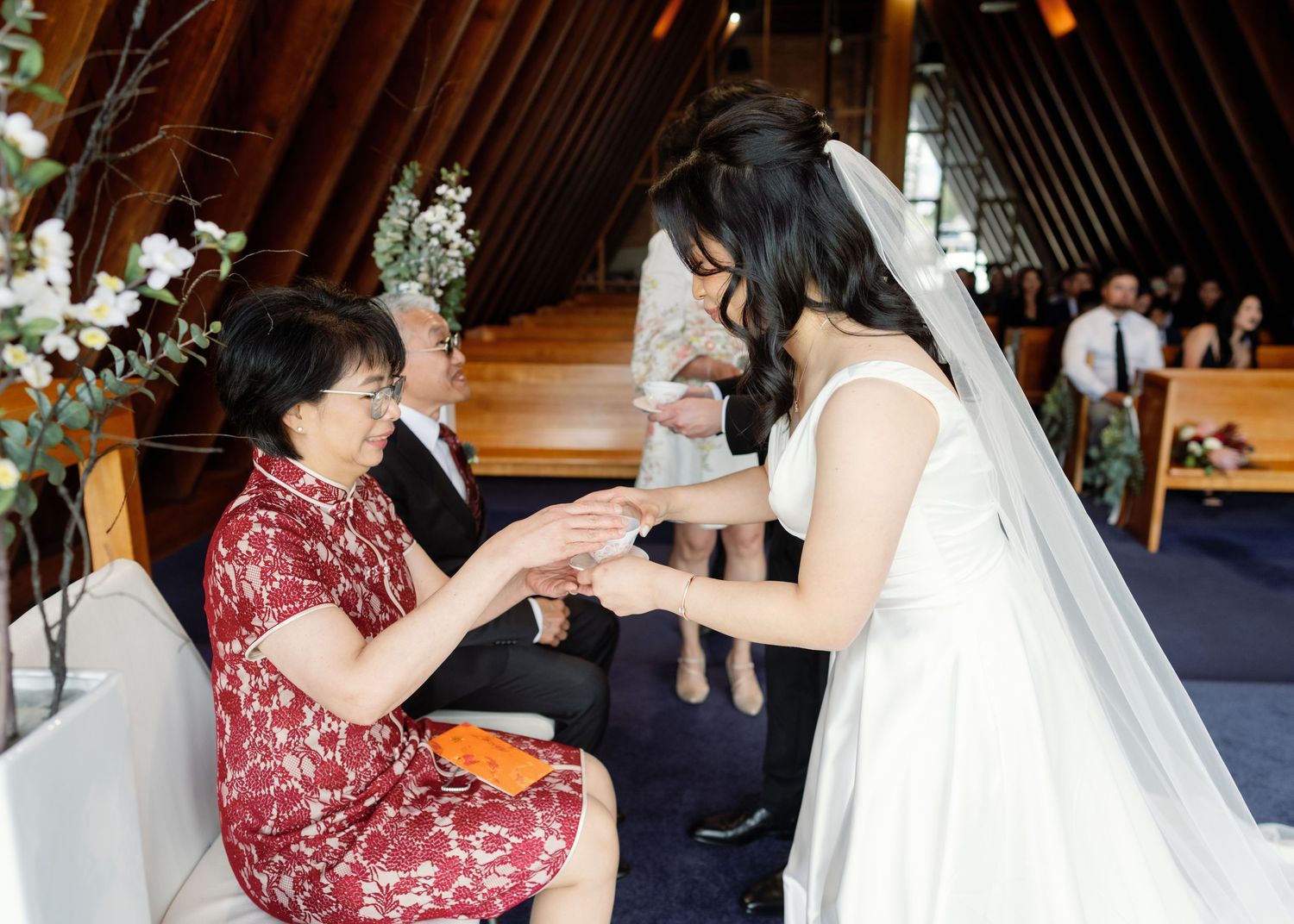 A wedding party member in burgundy dress helps adjust the bride's gown during preparation.