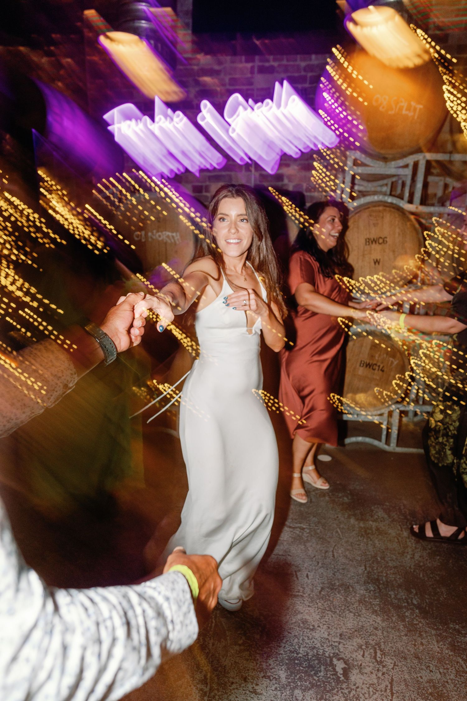 Wedding guests dancing on a dark dance floor illuminated by purple and gold lights.