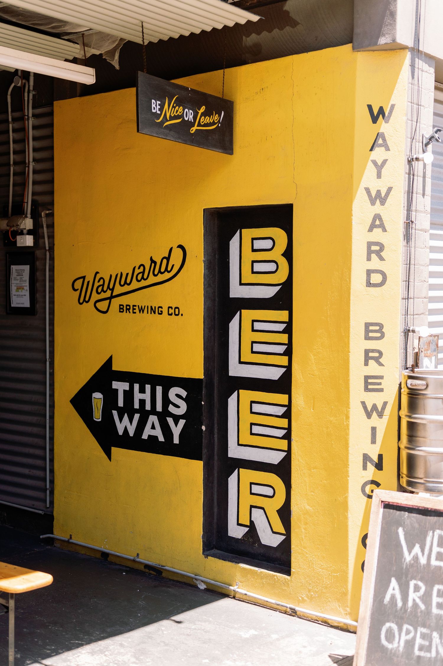 Yellow and black brewery signage with directional arrows and 'WAY' text on industrial walls.