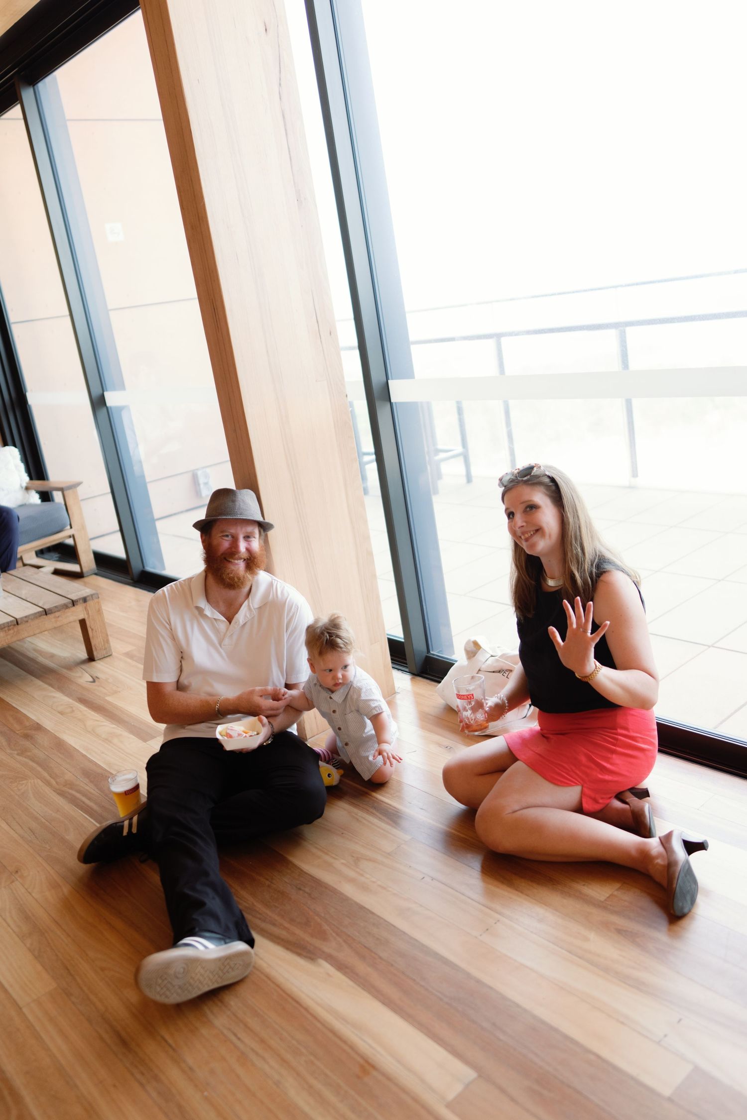 Group sitting casually on hardwood floor in modern space with large windows.