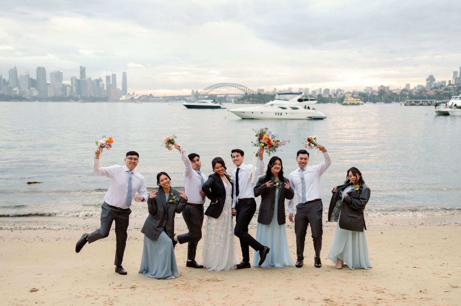 A celebratory group jumping on a beach with boats and city skyline in the background.