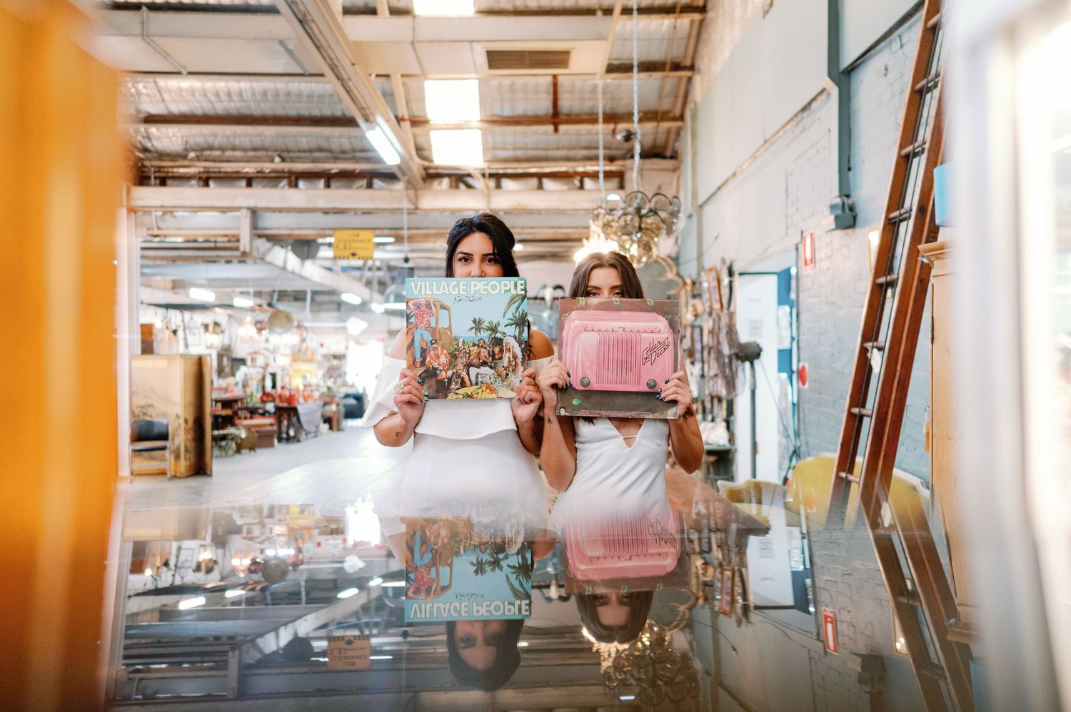 A reflection in a mirrored surface shows someone sitting at a counter in an industrial-style space.
