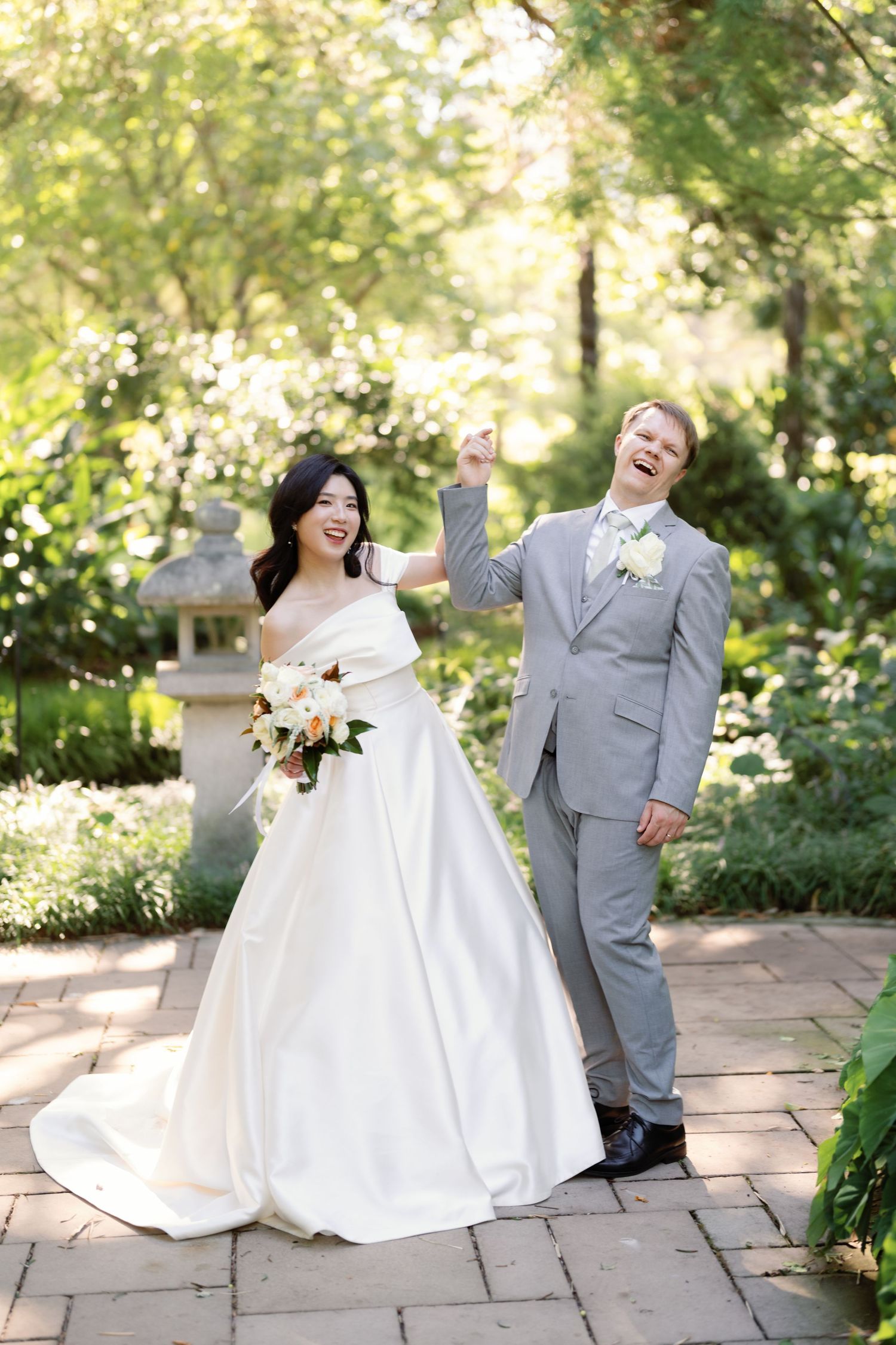 Wedding couple poses playfully on stone patio with greenery in background during outdoor photo session.