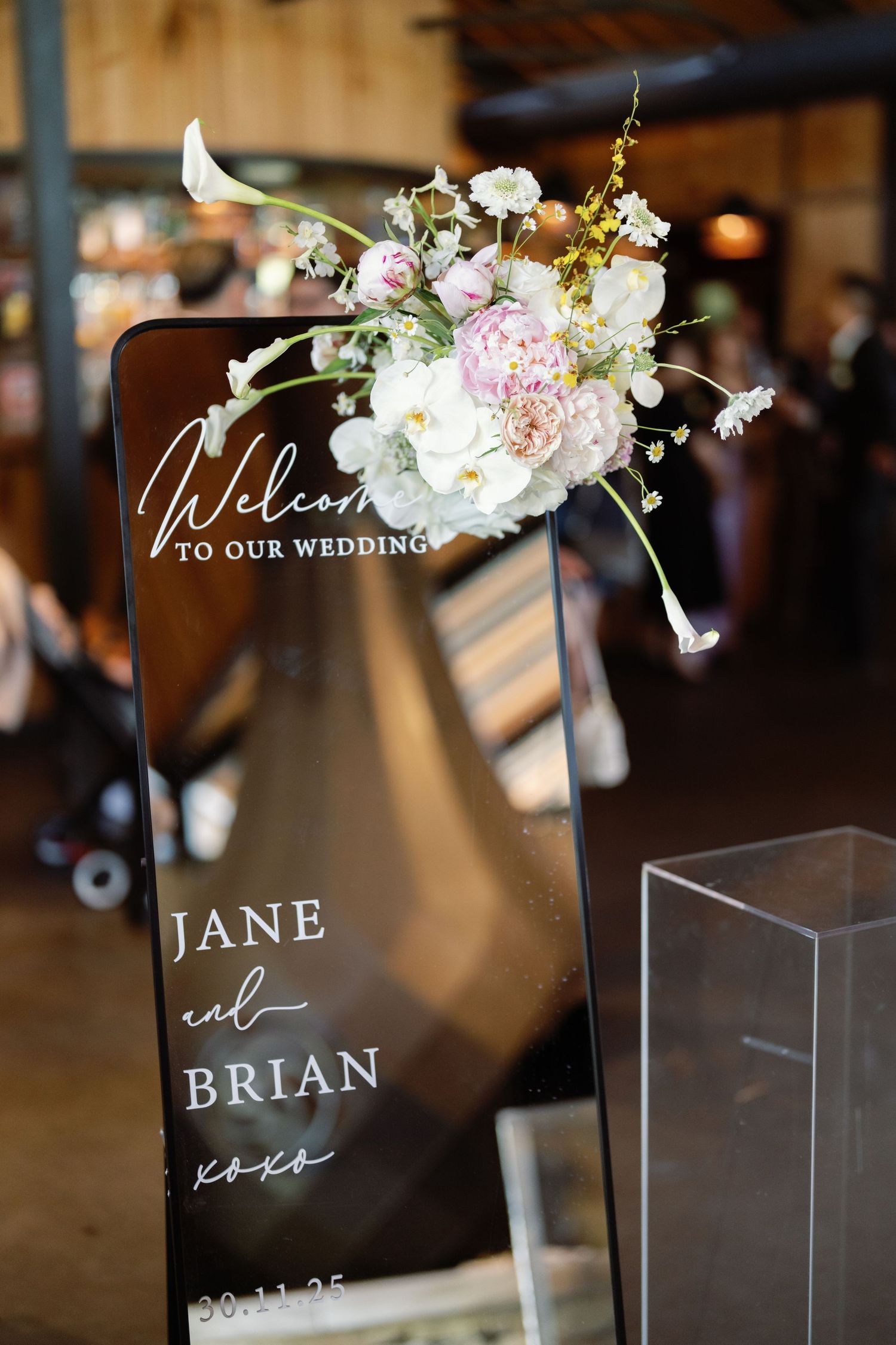 Modern acrylic wedding welcome sign decorated with pink and white floral arrangement.