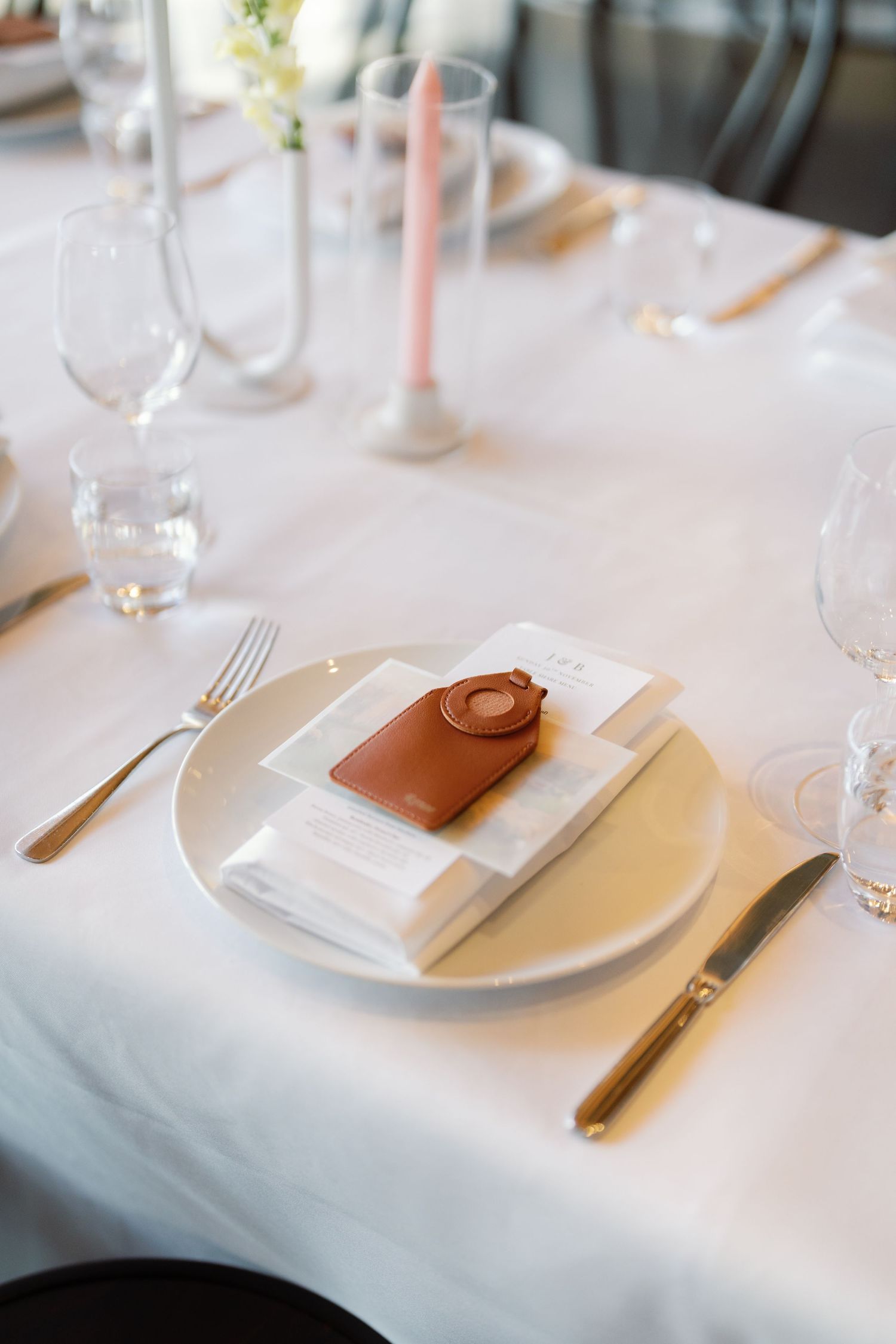 Elegant white table setting with silverware and leather menu holder at formal reception.