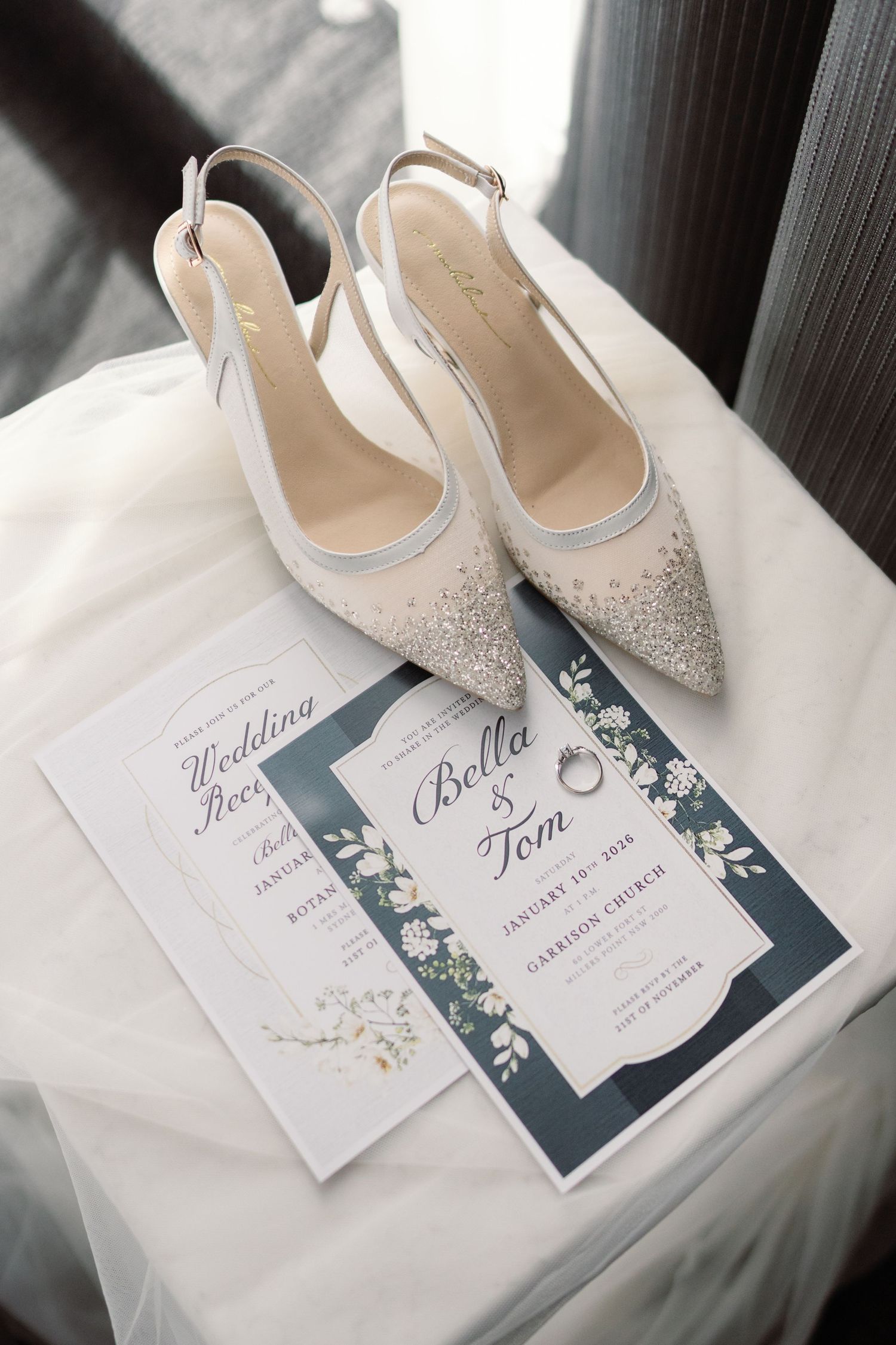 Sparkly bridal shoes next to wedding invitations and stationery in navy blue and white colors.