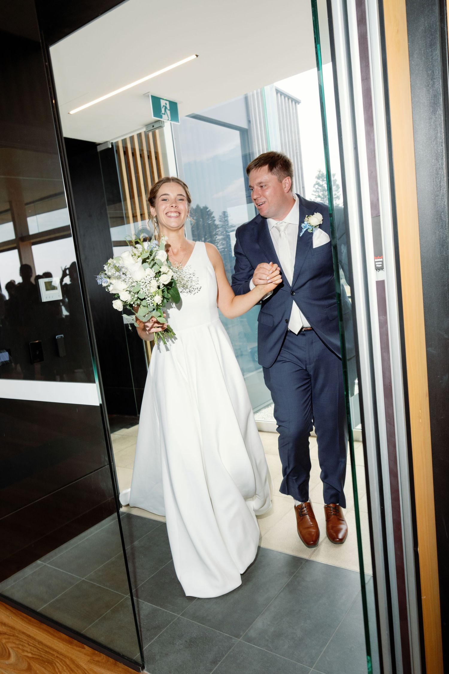 Wedding couple sharing joyful moments in a modern venue with glass walls and wooden floors.