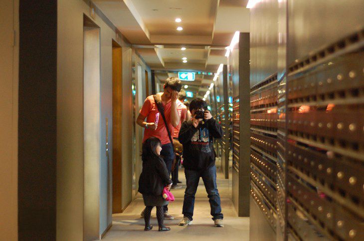 People walking through a brightly lit hallway corridor with wooden panels and fluorescent lighting.