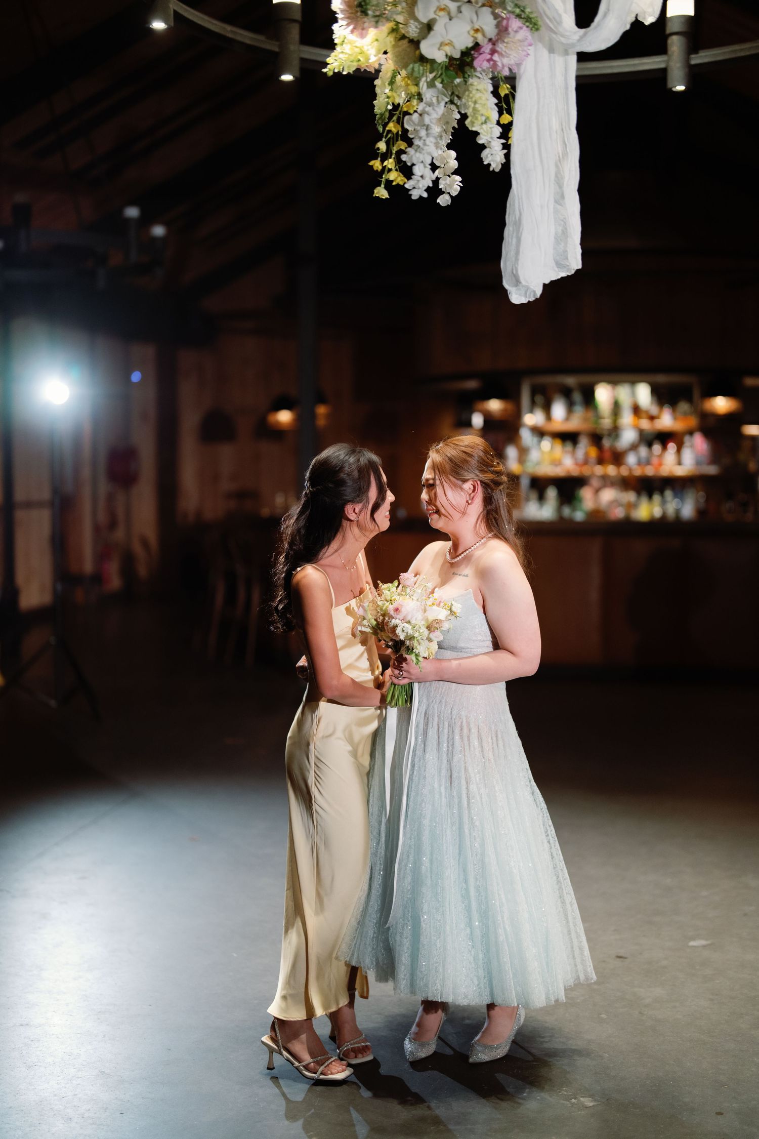 Two people dancing together under hanging floral decorations in a dimly lit venue.