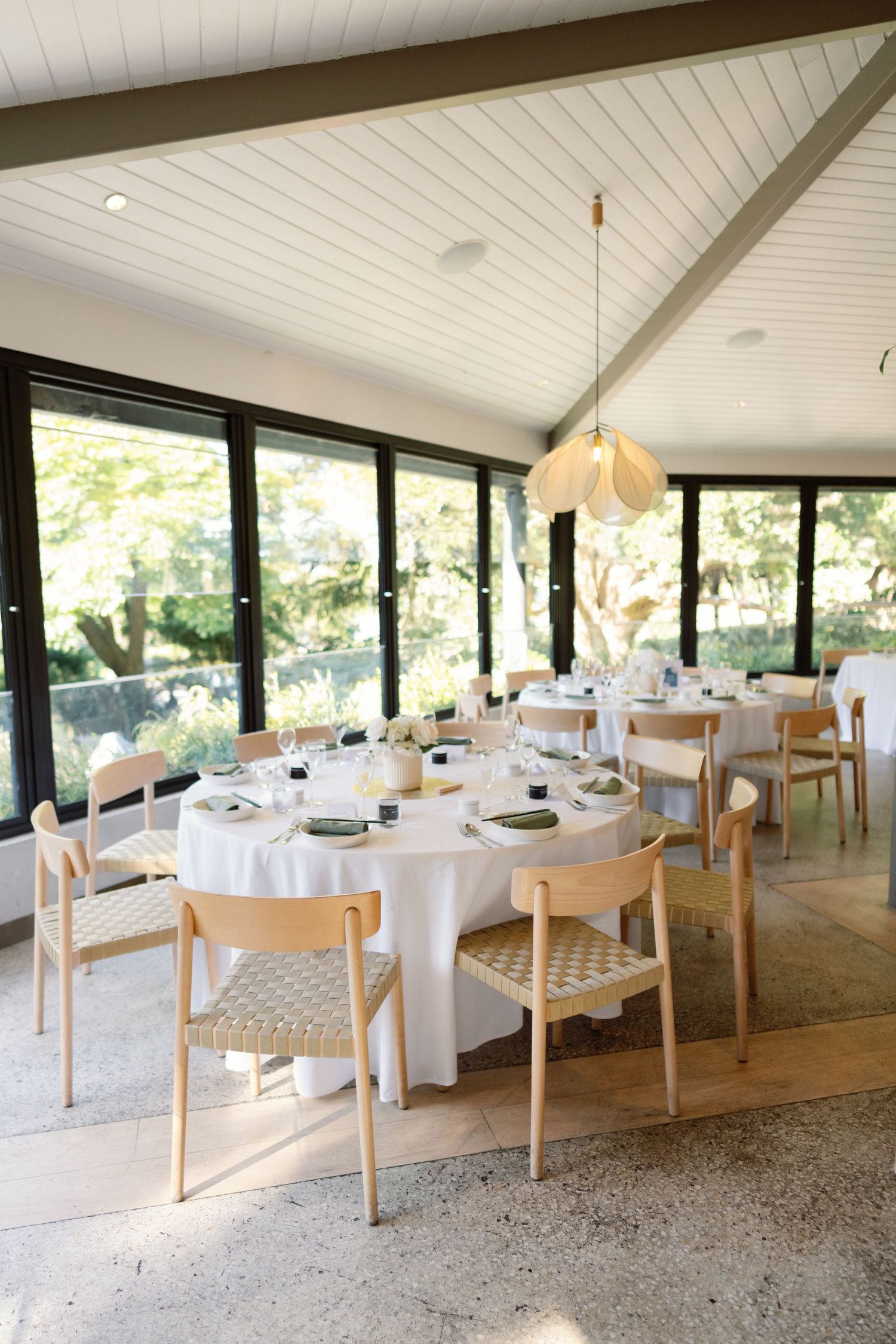 Modern reception venue with white tablecloths and natural wood chairs under vaulted ceiling.