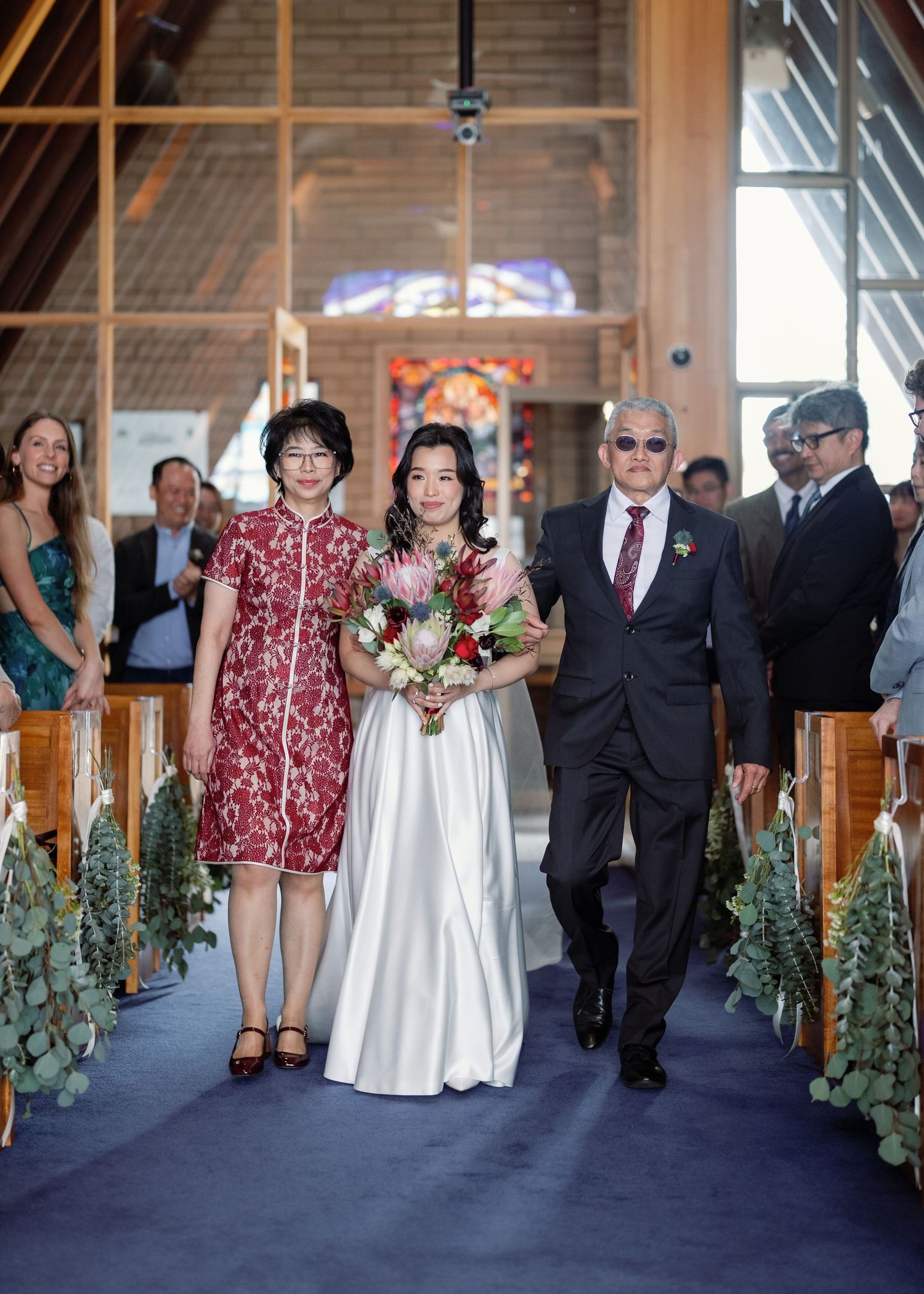 Wedding ceremony processional in church with evergreen decorations along wooden pews.