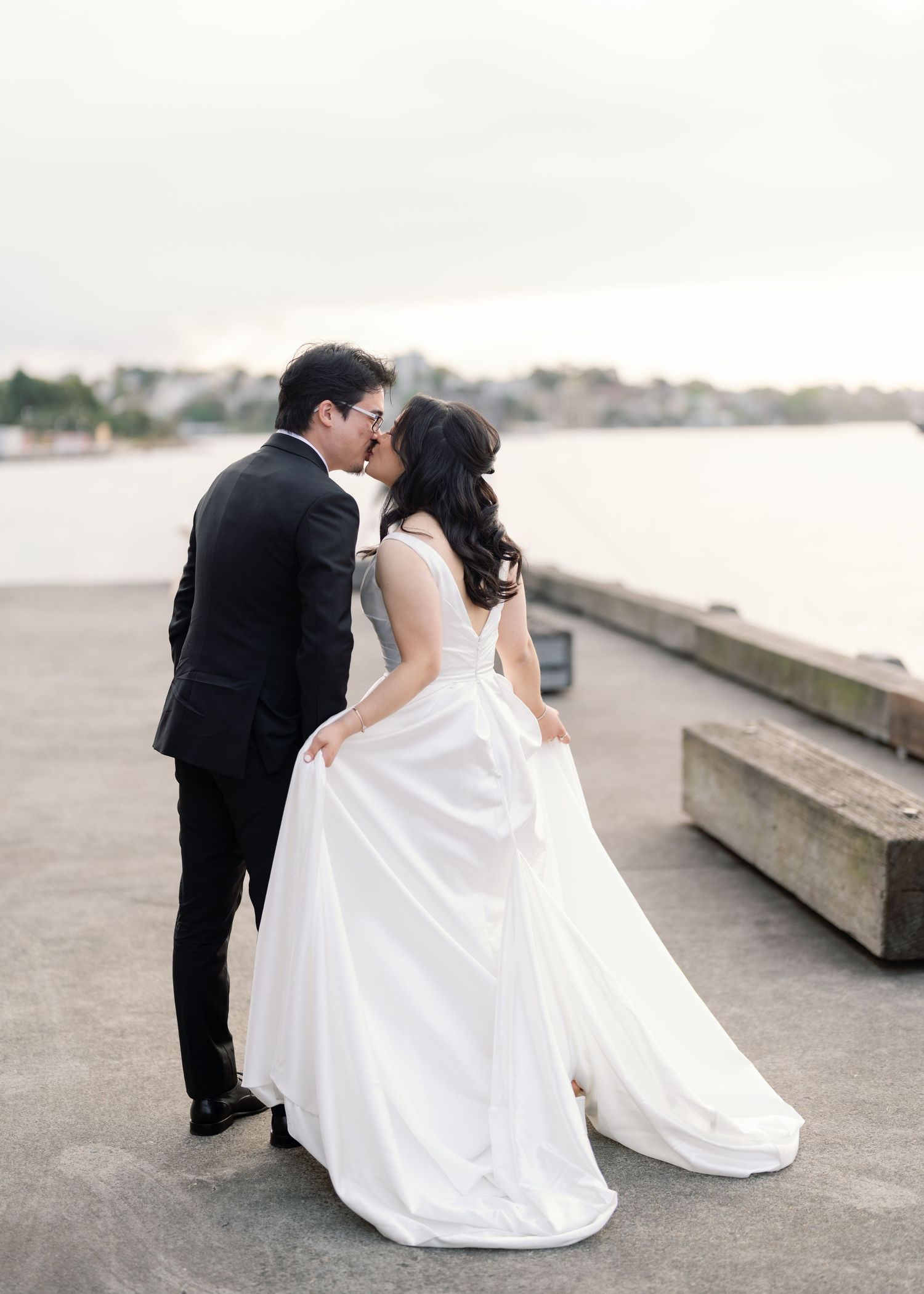 Wedding couple shares romantic moments along a waterfront walkway with flowing white dress.