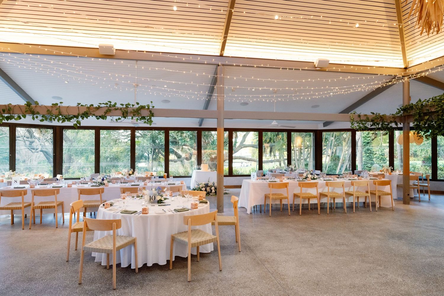 Elegant wedding reception venue with fairy lights, round tables, wooden chairs, and garden views.