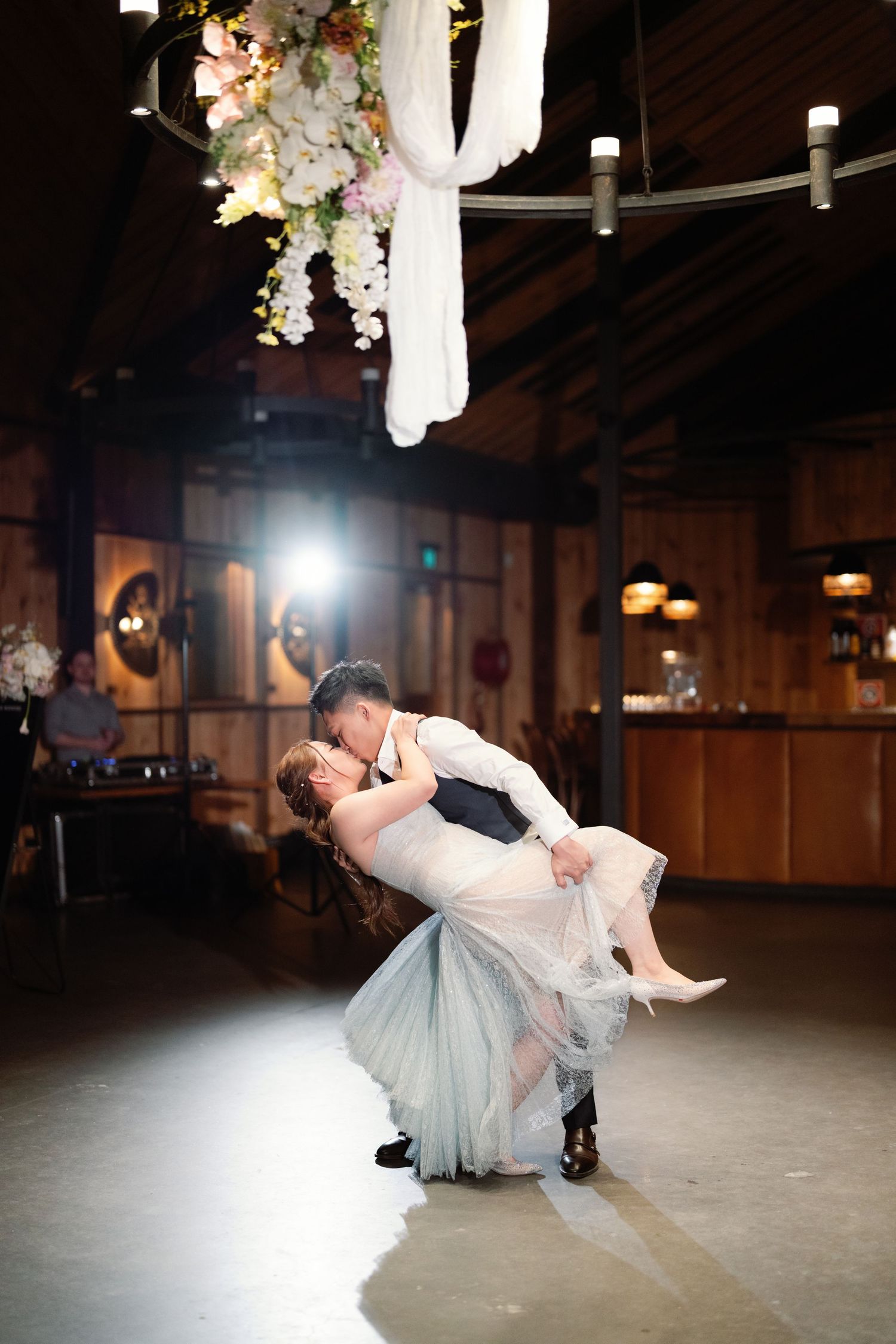 Dramatic dance dip on reception floor with spotlights and floral decorations overhead.