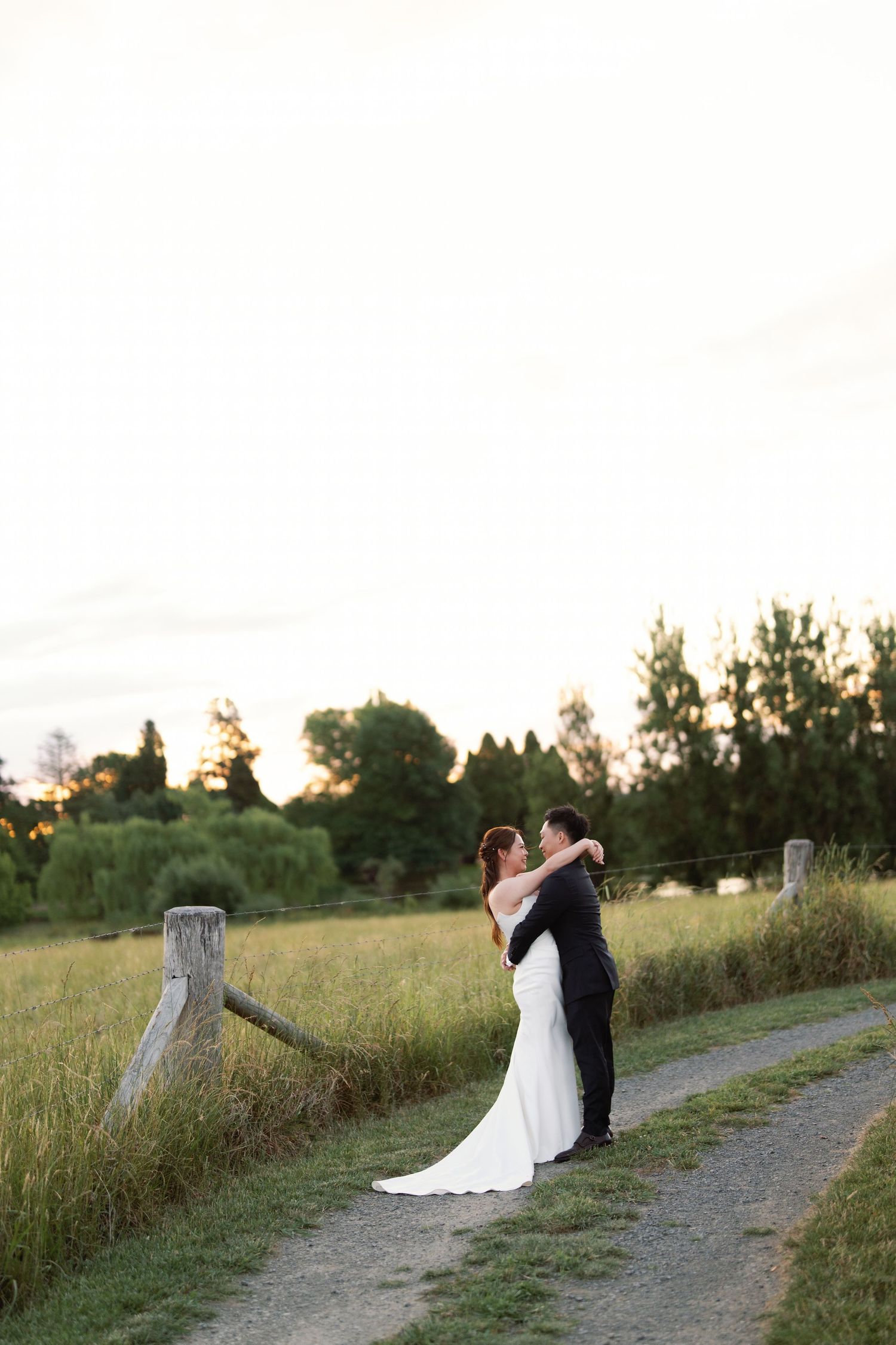 Couple shares romantic moment on rustic path during sunset wedding photoshoot.