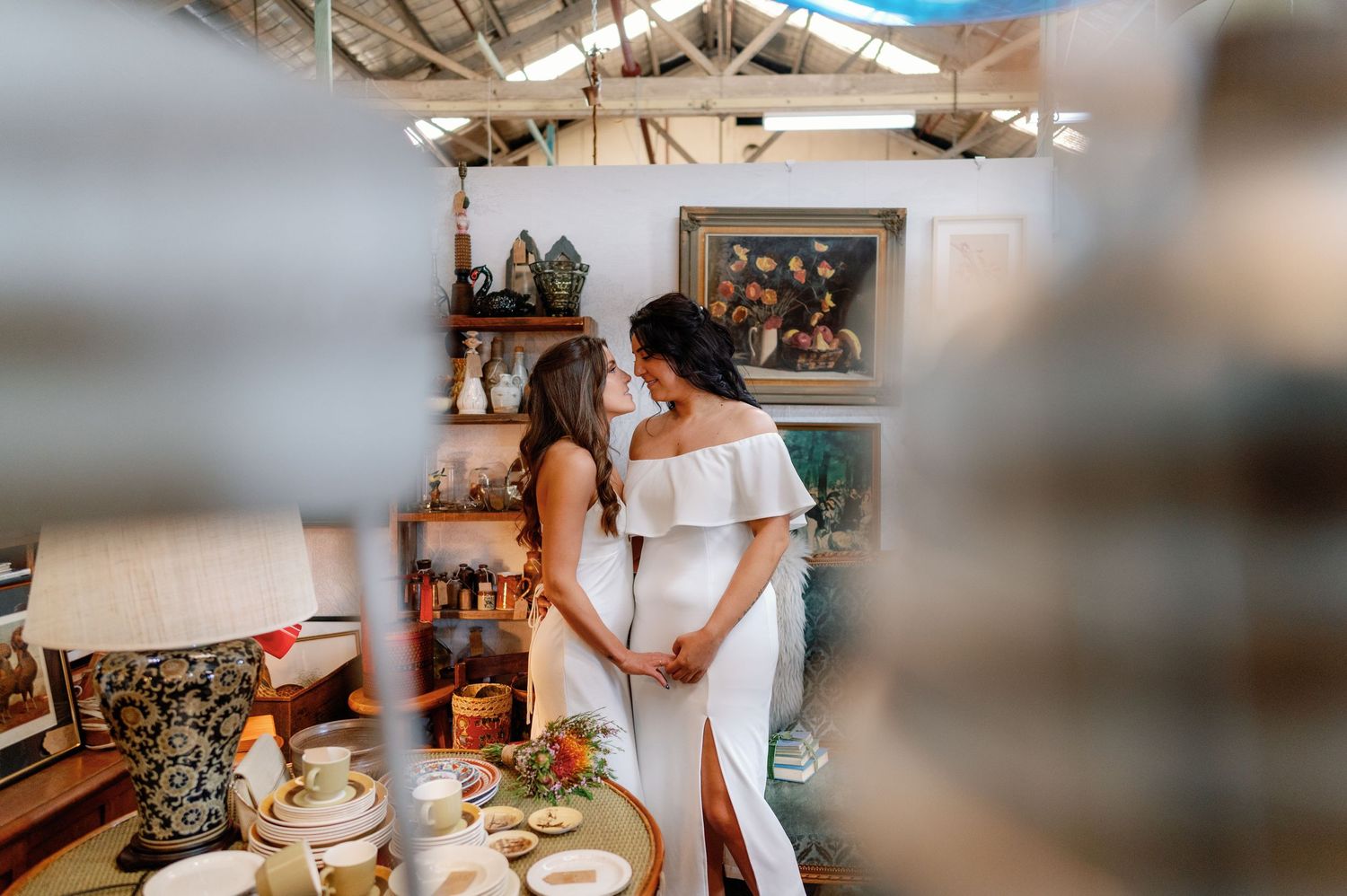 Two friends in white outfits share a joyful moment while preparing food in a bright kitchen setting.