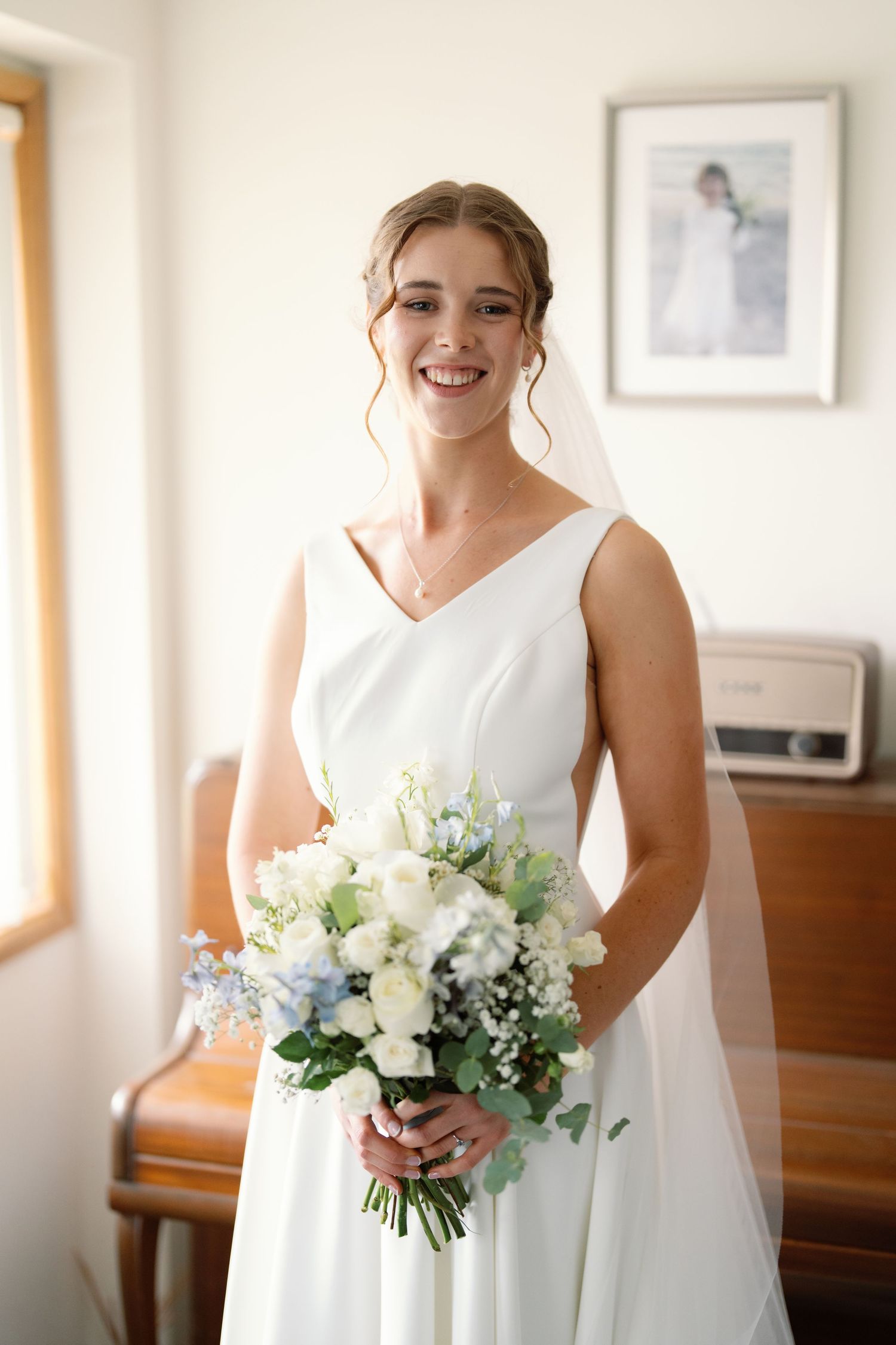 Elegant white bridal bouquet with fresh flowers and greenery against a simple indoor backdrop.