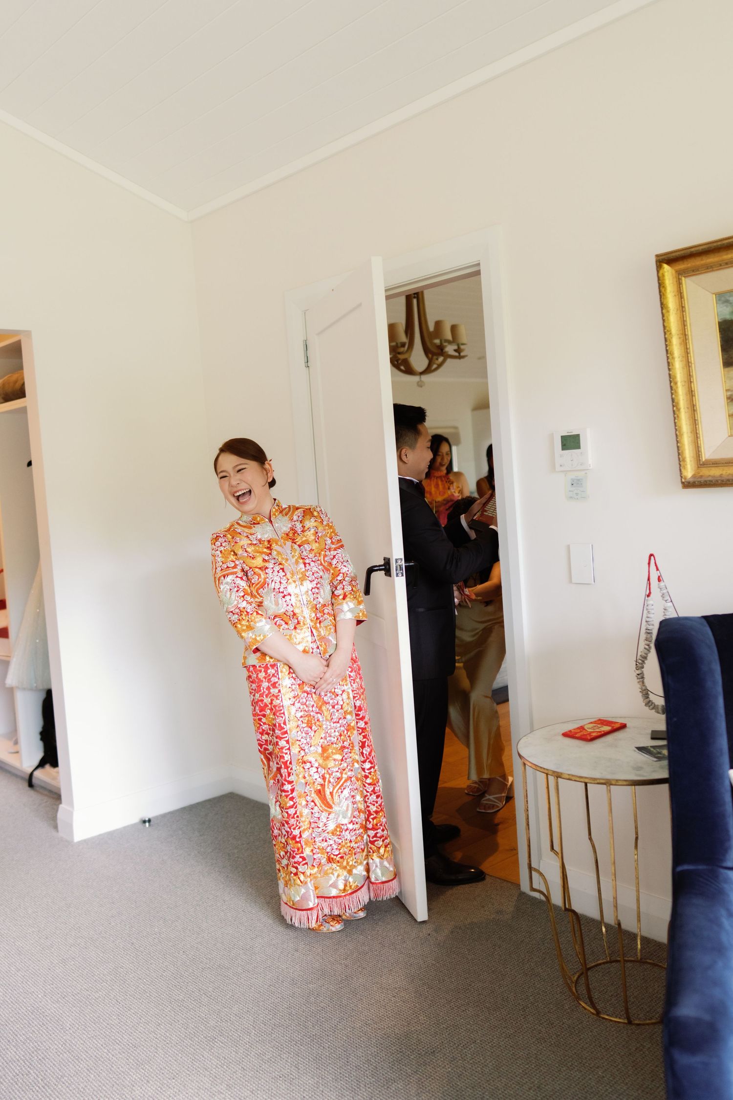 A person in a vibrant orange floral dress stands laughing in a bright room.