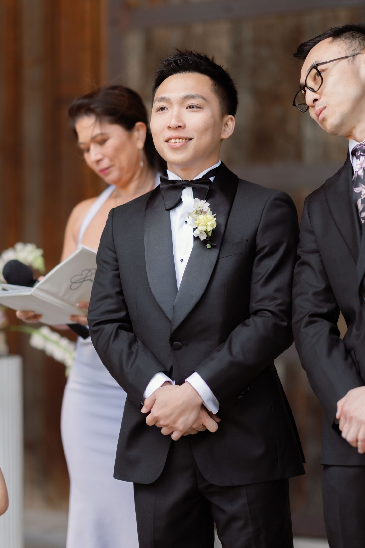 Groomsmen in black tuxedos stand in a line during a formal wedding ceremony.