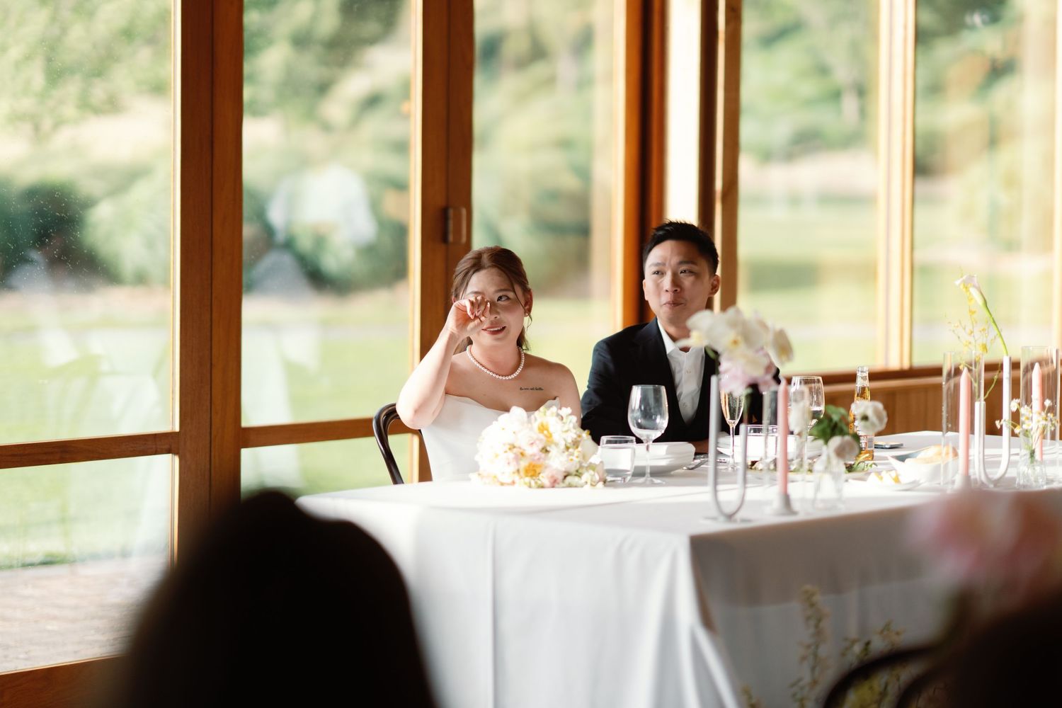 Wedding reception venue with elegant table settings and large windows overlooking nature.