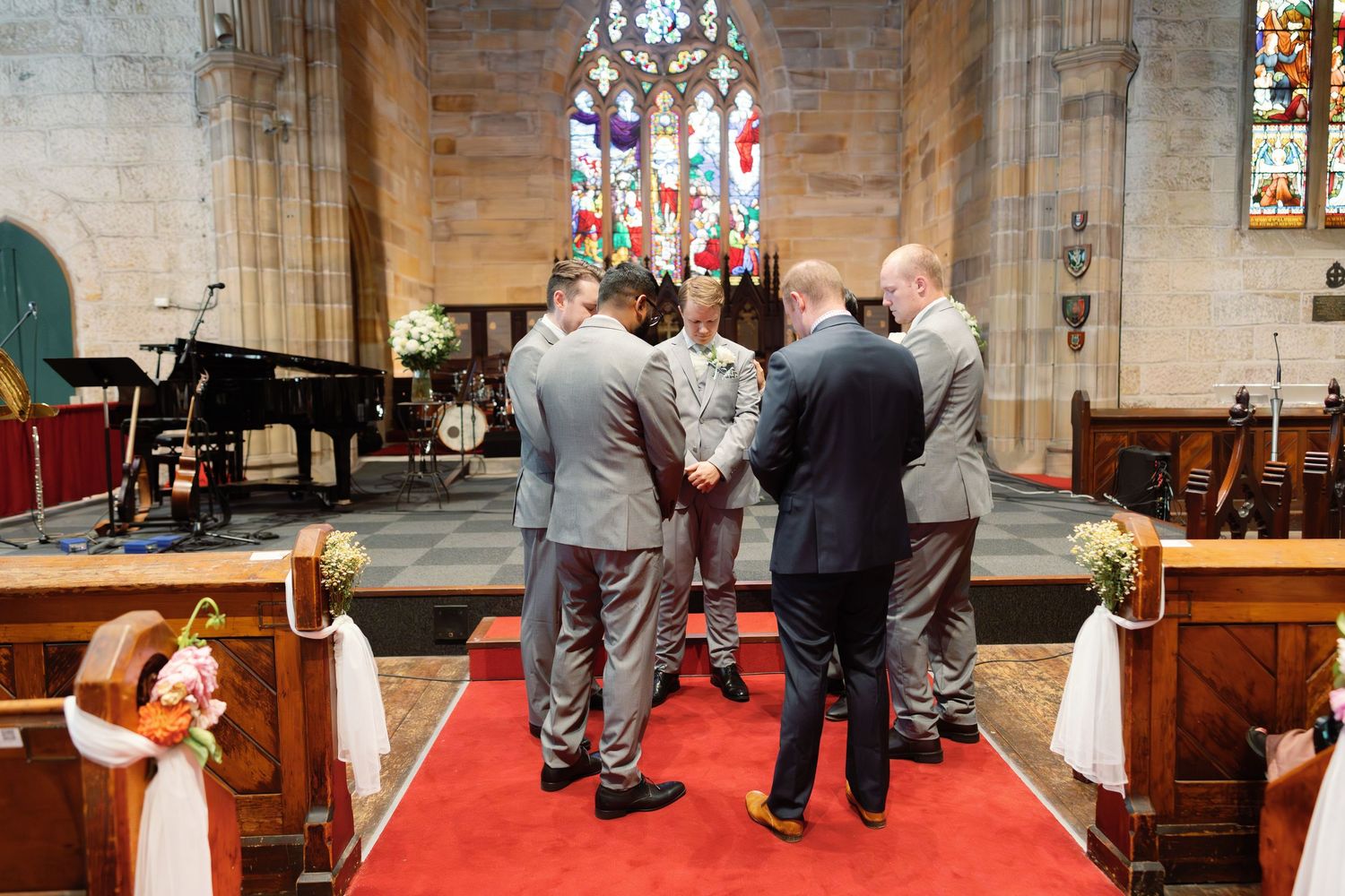 Church wedding ceremony with guests seated in wooden pews under stained glass windows.