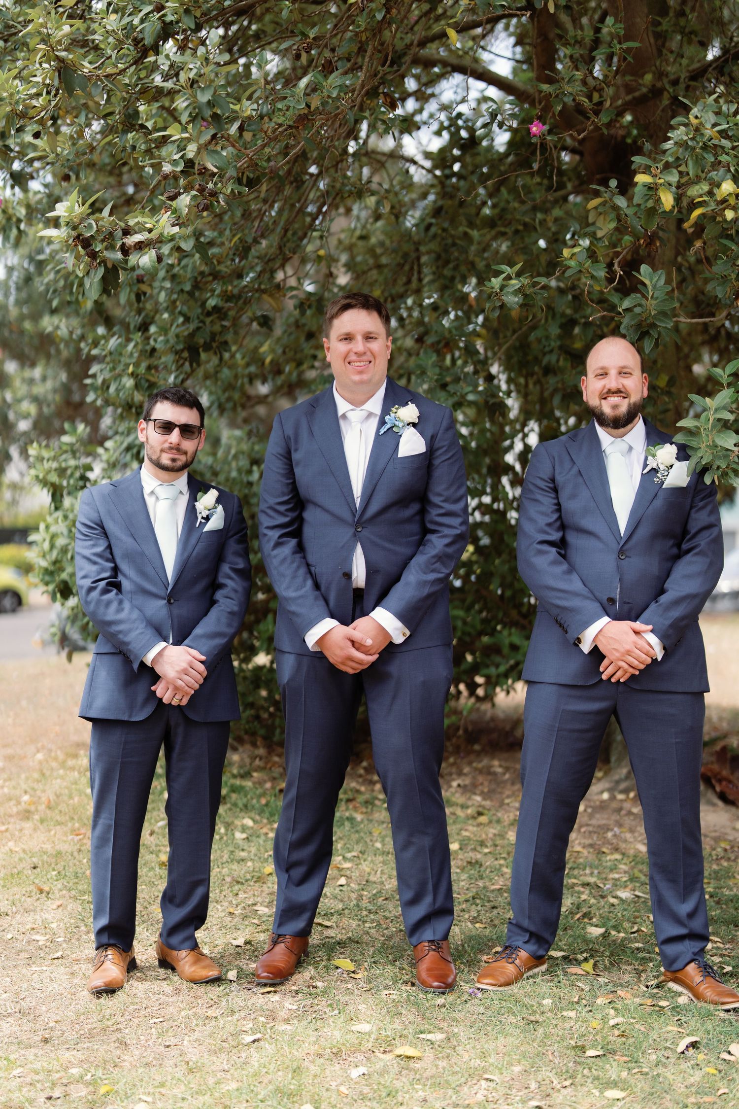 Groomsmen in matching navy suits and brown shoes posed casually outdoors.
