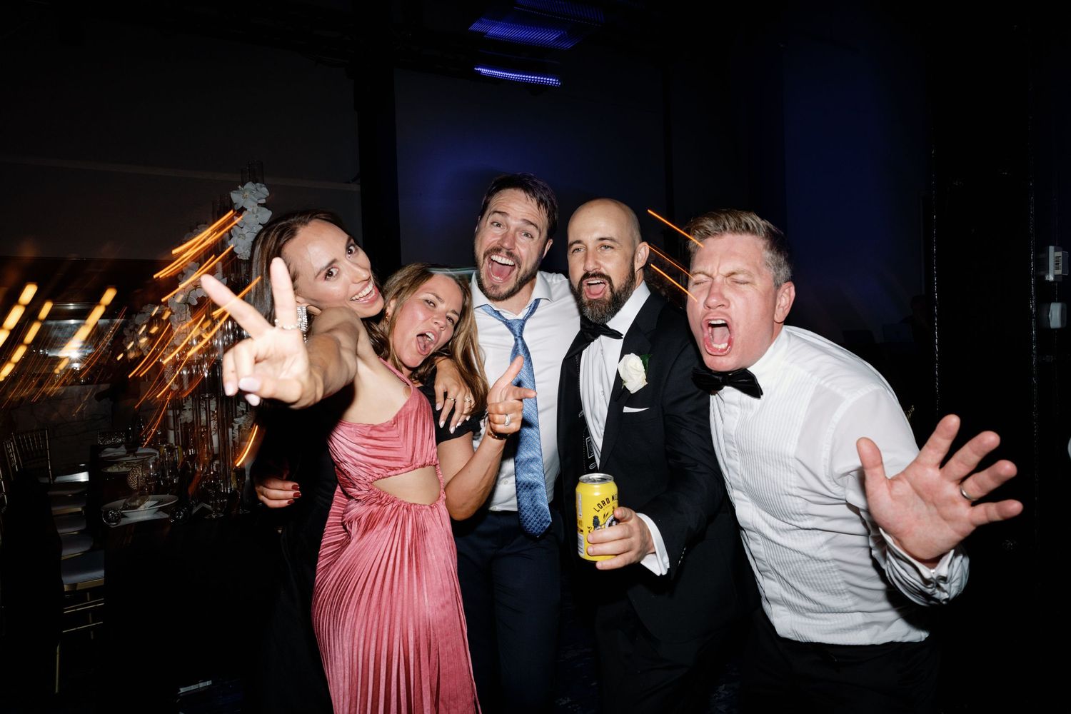 Wedding party guests posing energetically for a fun group photo at a reception.