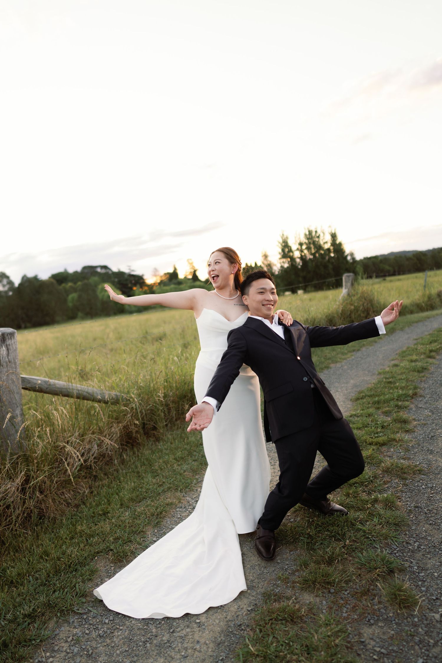 A couple striking dramatic poses on a gravel path at sunset.