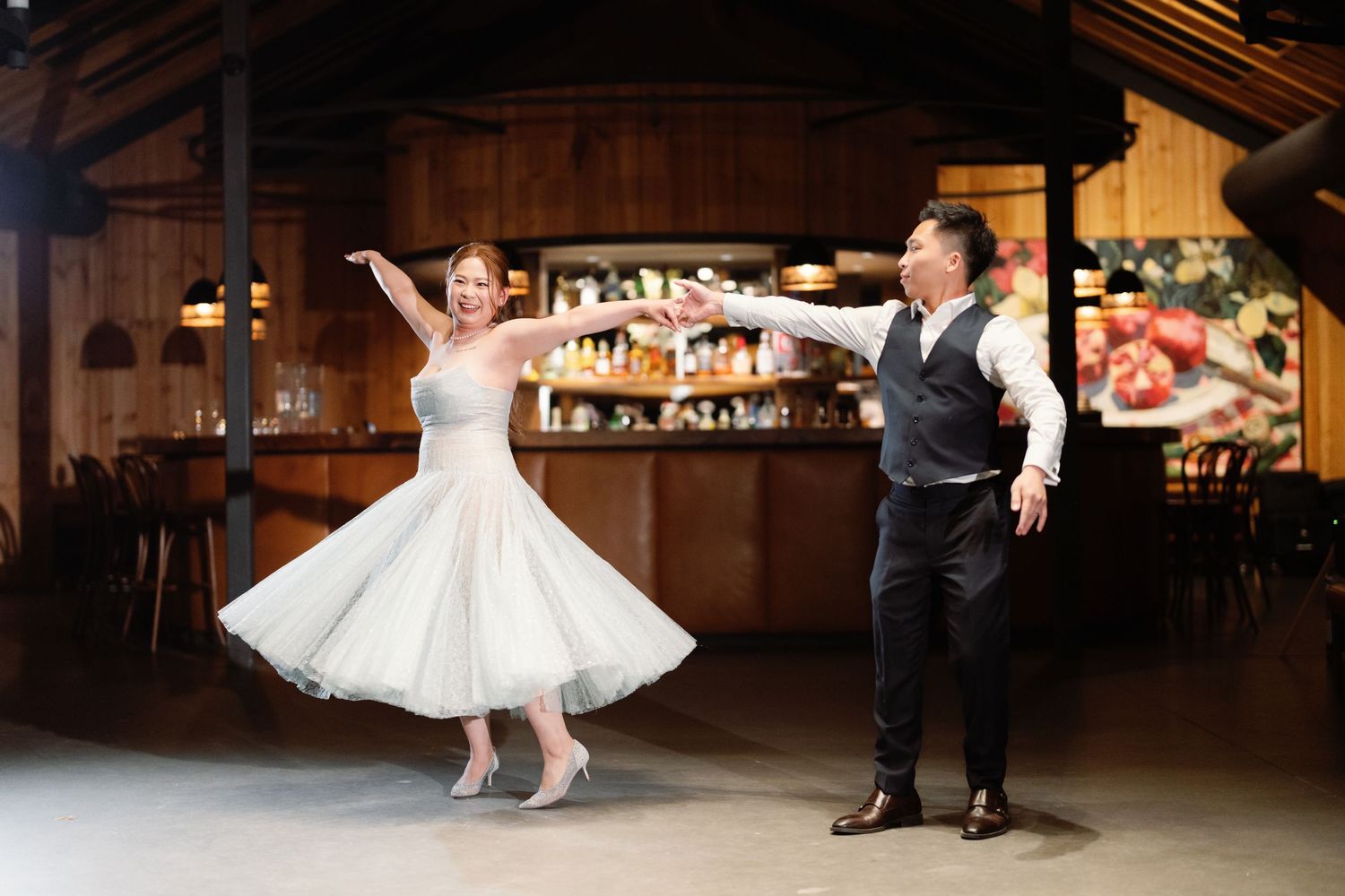 Joyful dance moment captured in rustic barn reception venue with wooden walls and warm lighting.