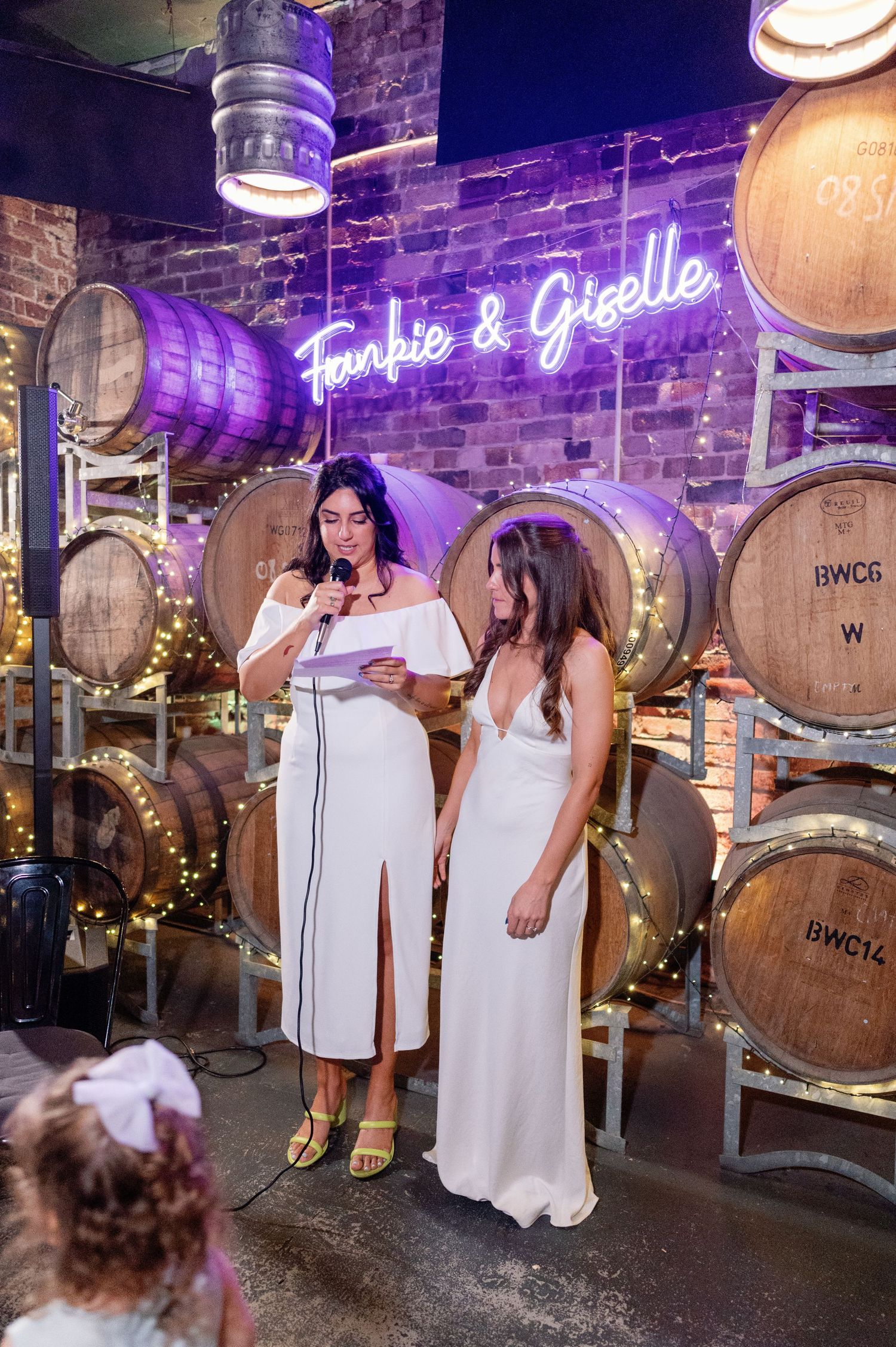 A celebratory scene unfolds in front of rustic wine barrels with purple neon accents.