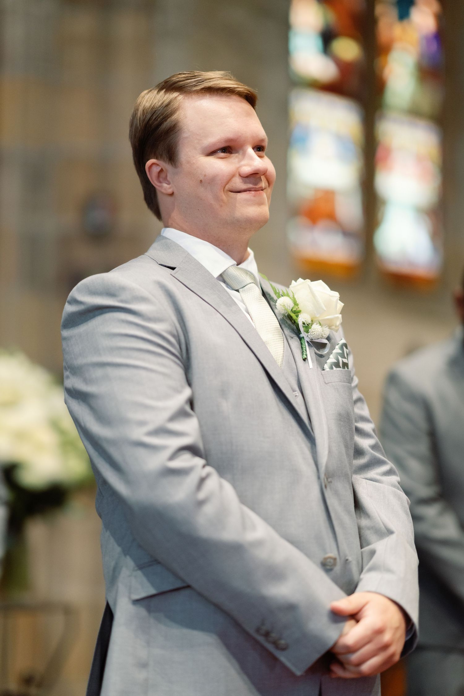 A groom in a light gray suit with boutonniere smiles during the ceremony.