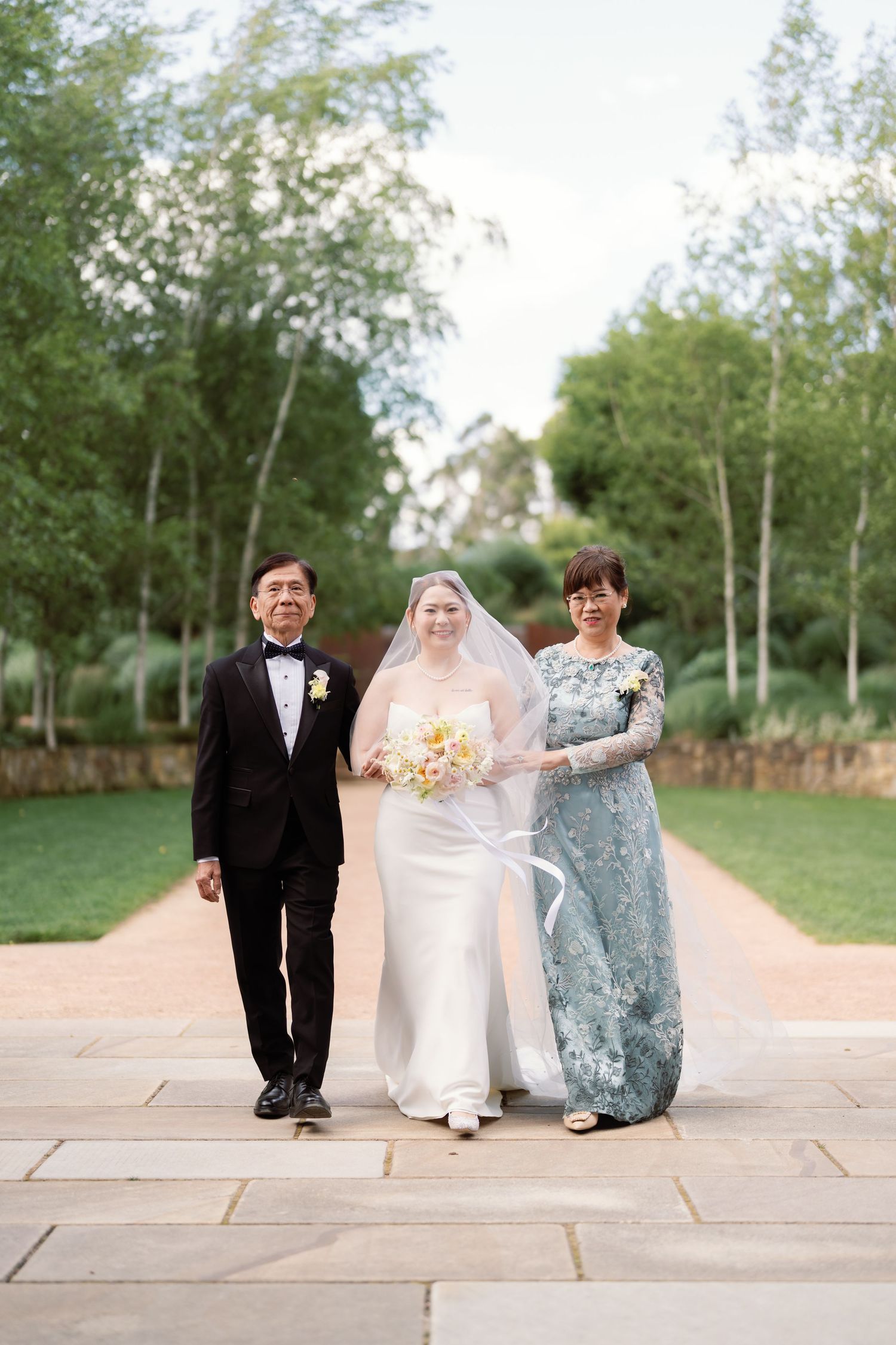 Wedding party members sit together on stone steps in an outdoor garden setting.