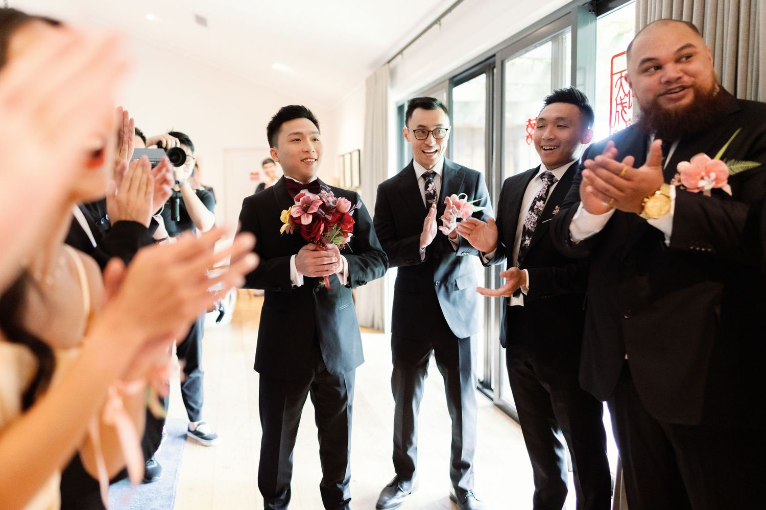 Group of formally dressed wedding guests celebrating and dancing together indoors.