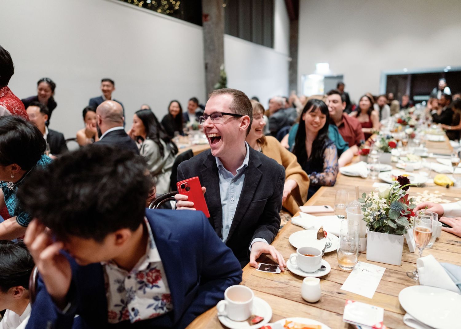 A panoramic view of wedding reception guests seated at long tables in a modern white venue space.