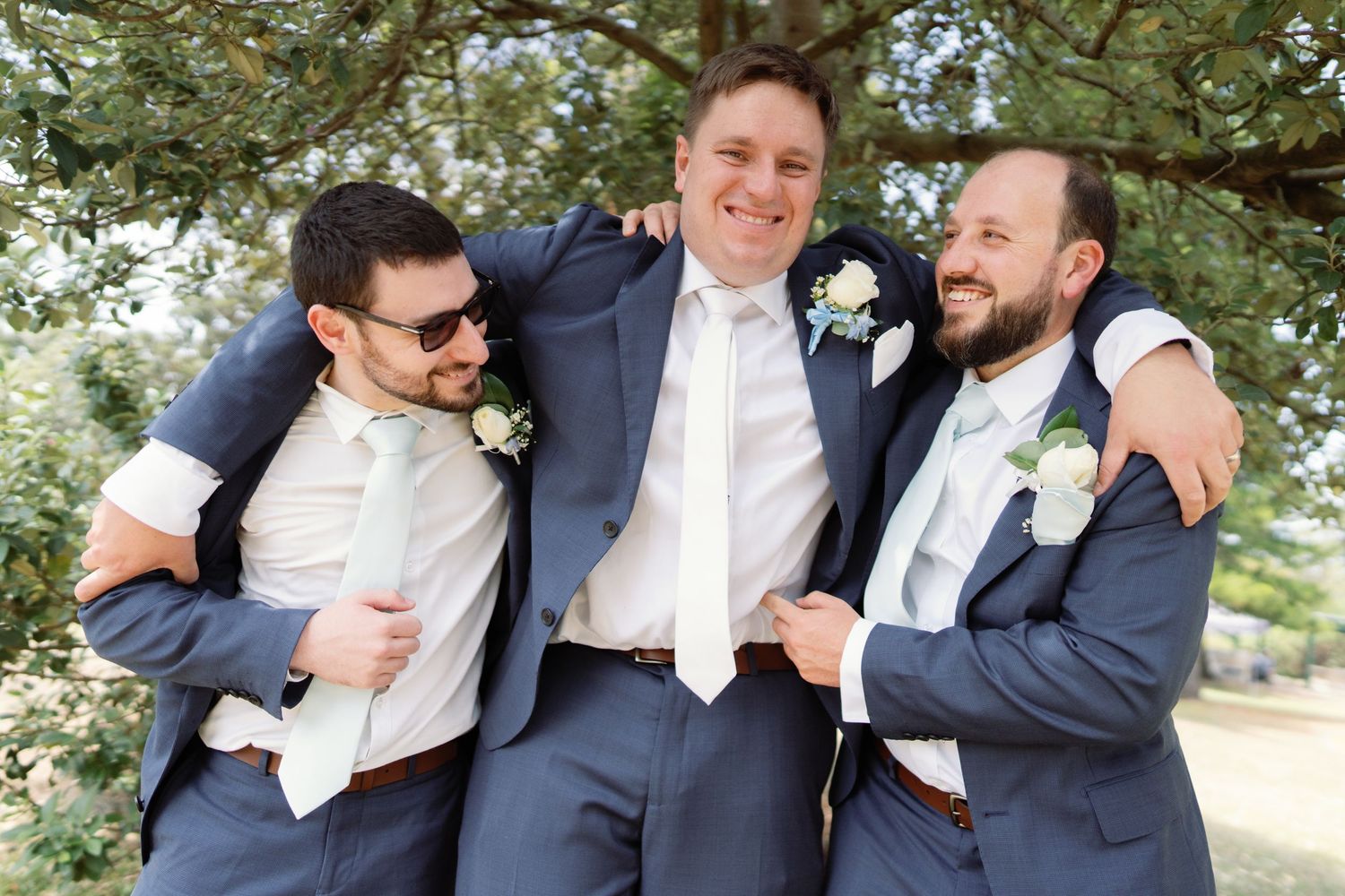 Groomsmen in navy suits sharing laughs outdoors.