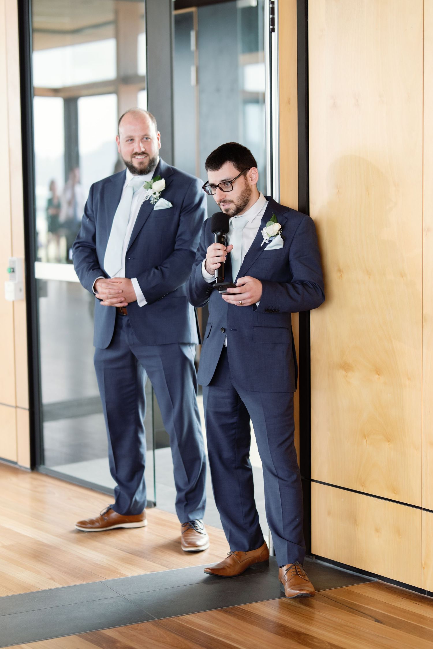 Groomsmen in navy suits checking phones in modern hallway.