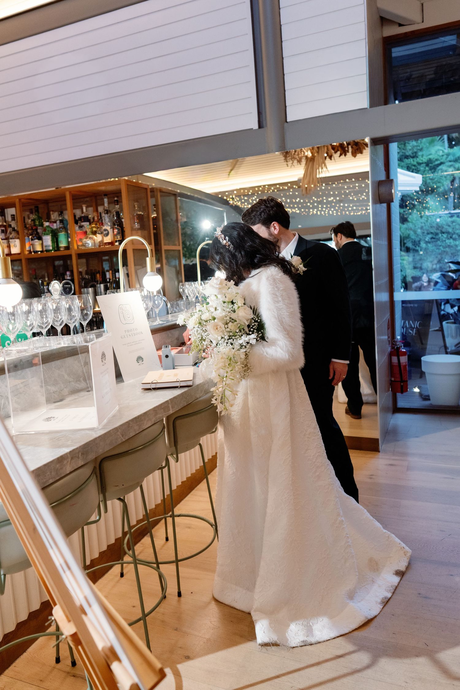 Bride and groom share a kiss near a bar inside a modern wedding venue.