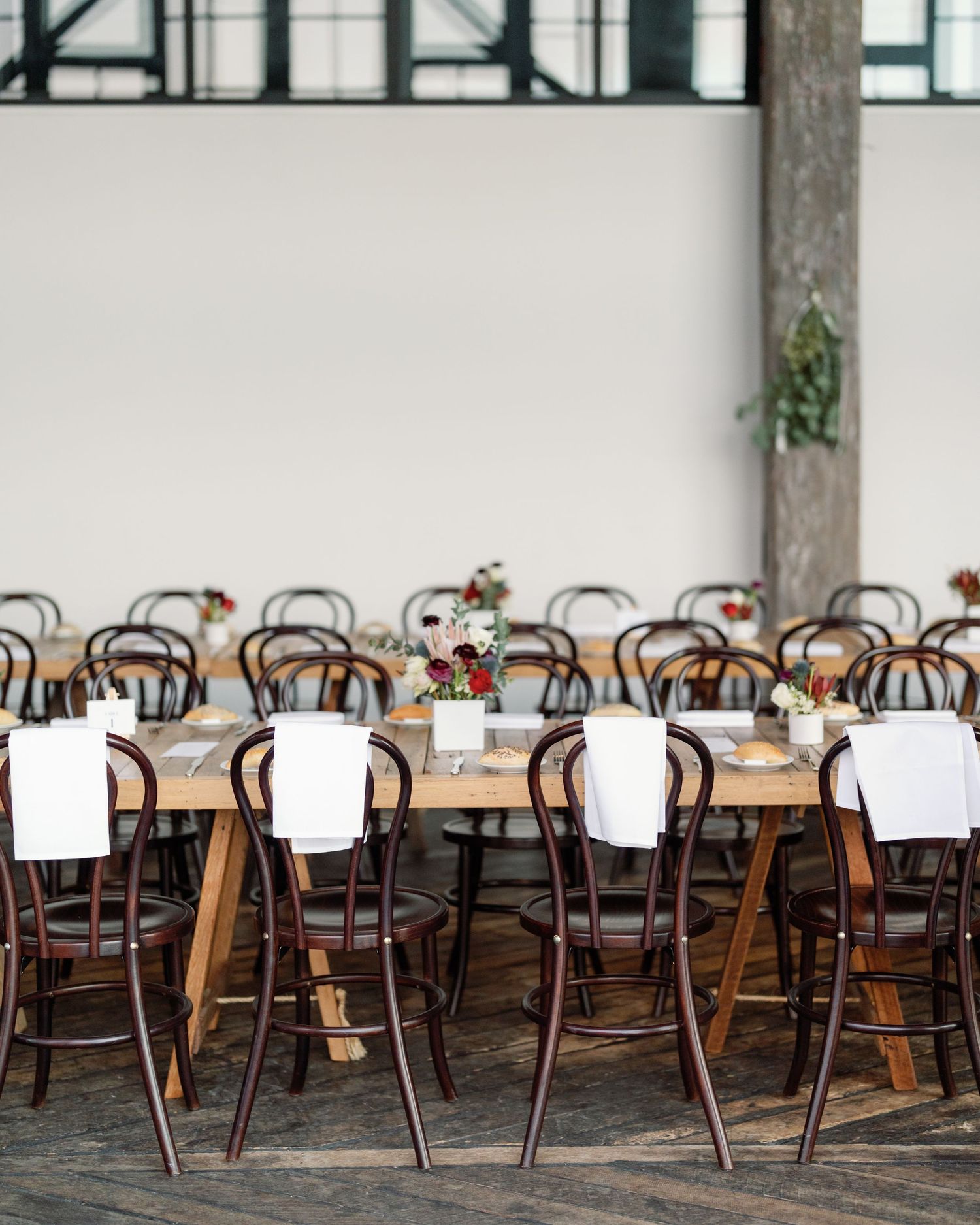 Reception venue with rows of wooden chairs and white tablecloths in an industrial space.