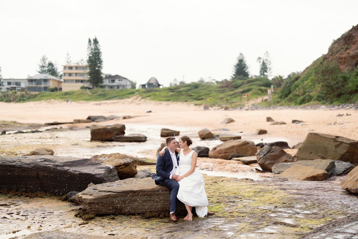 Wedding couple poses on rocky beach landscape during sunset.