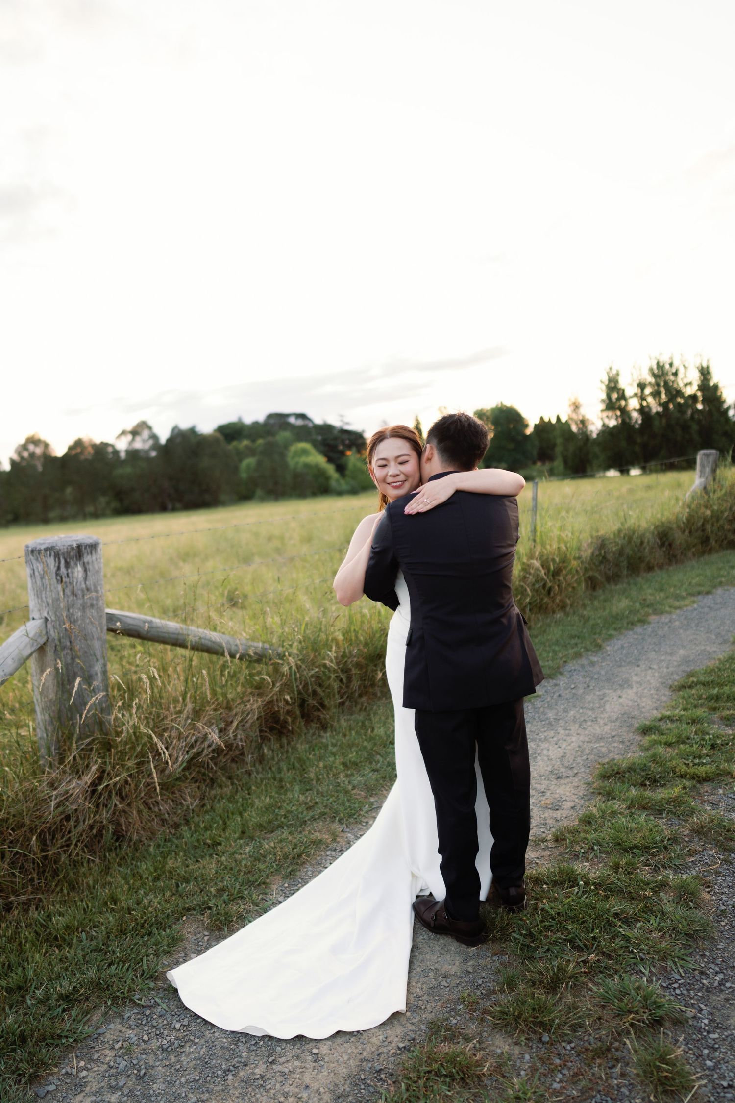 Intimate wedding couple moment on rustic dirt path surrounded by tall grass at sunset.