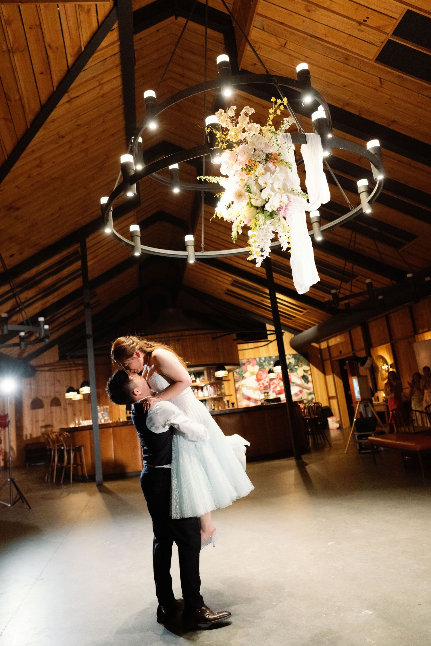 Romantic dance scene under wooden beams and twinkling lights at a reception venue.