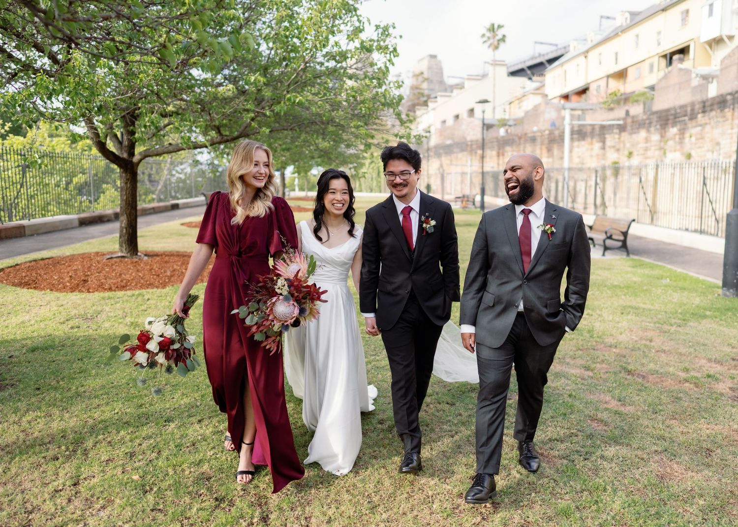 Wedding party walking outdoors on grassy area near stone buildings.